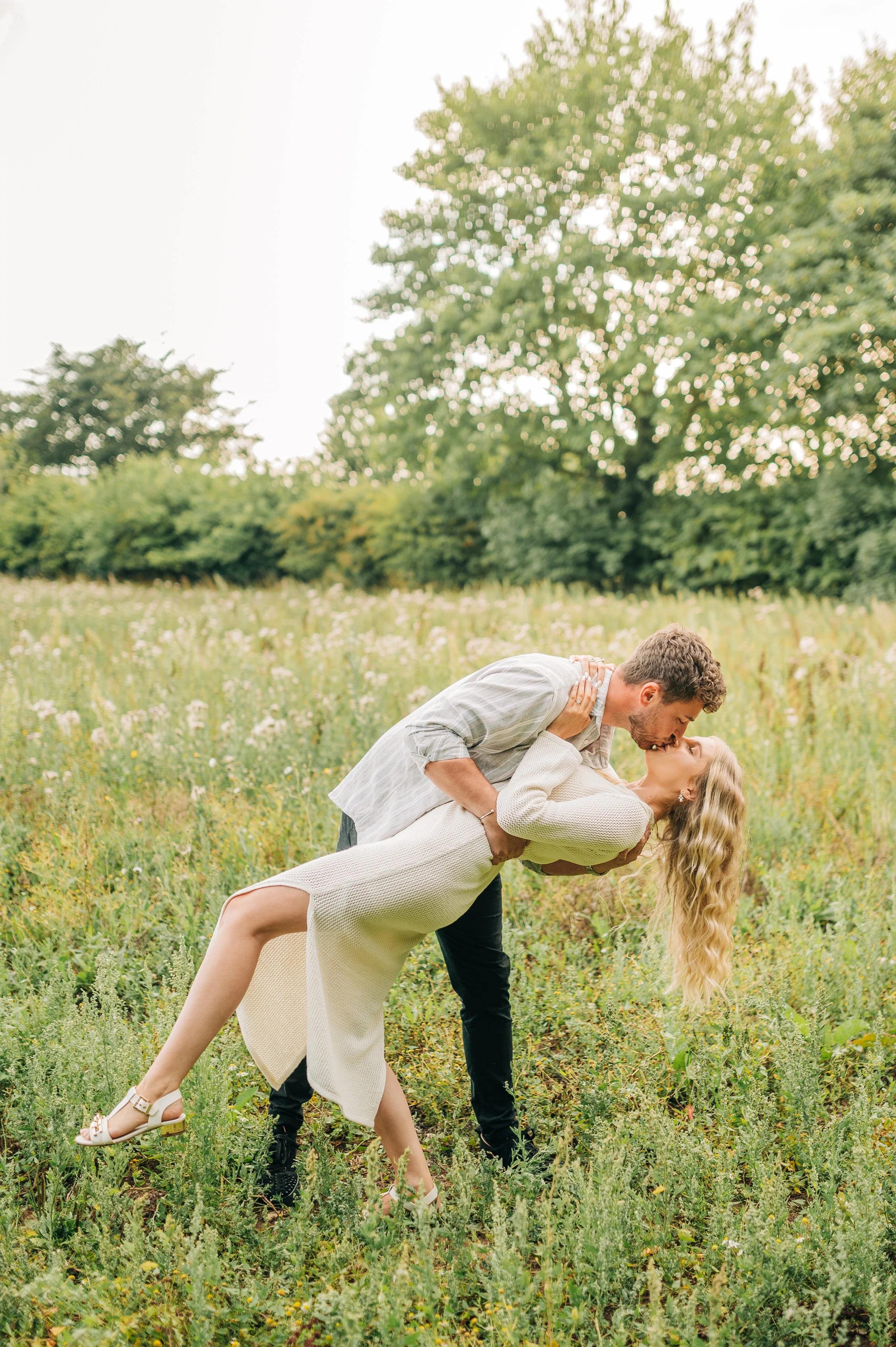 Norfolk Wedding Photographer.  A couple romantically dancing or posing in a grassy field with trees in the background, the man leaning over to kiss the woman who is leaning back.