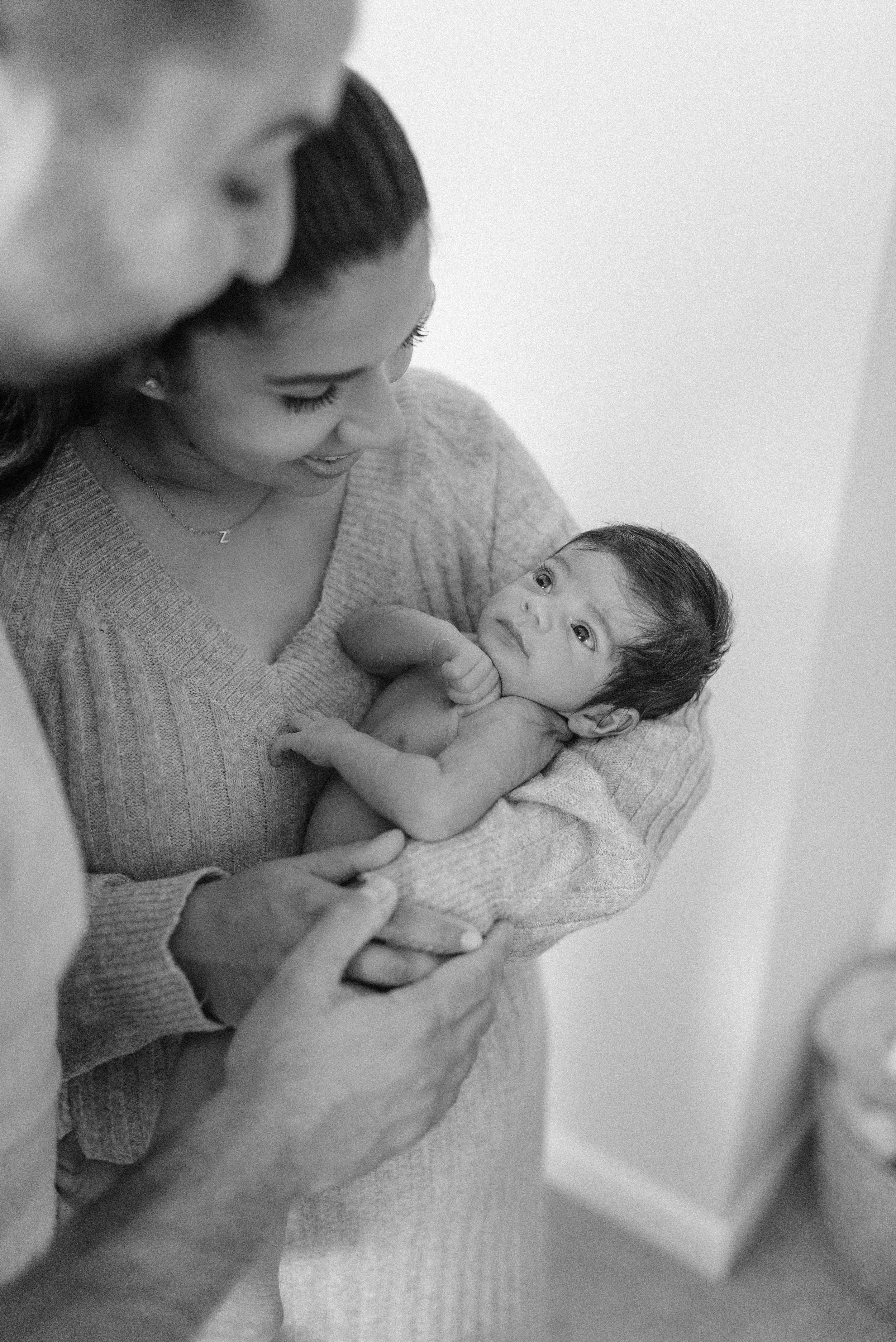 Norfolk Family Photographer.  A woman holding a newborn baby, looking at each other affectionately, in a black-and-white photograph.