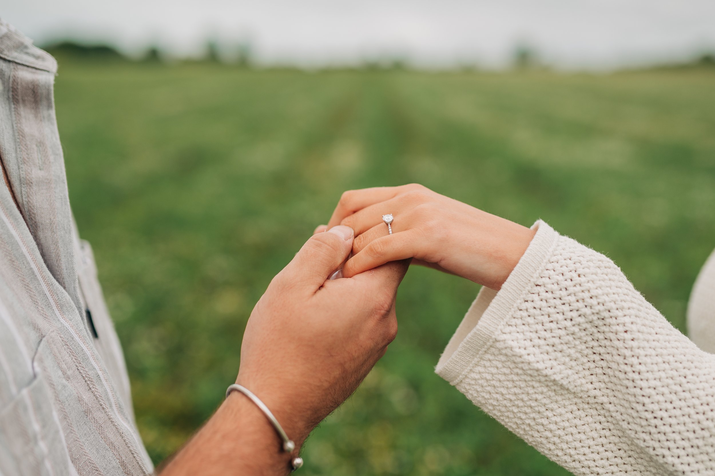 Norfolk Wedding Photographer.  A person placing a ring on another person's finger in an outdoor setting.