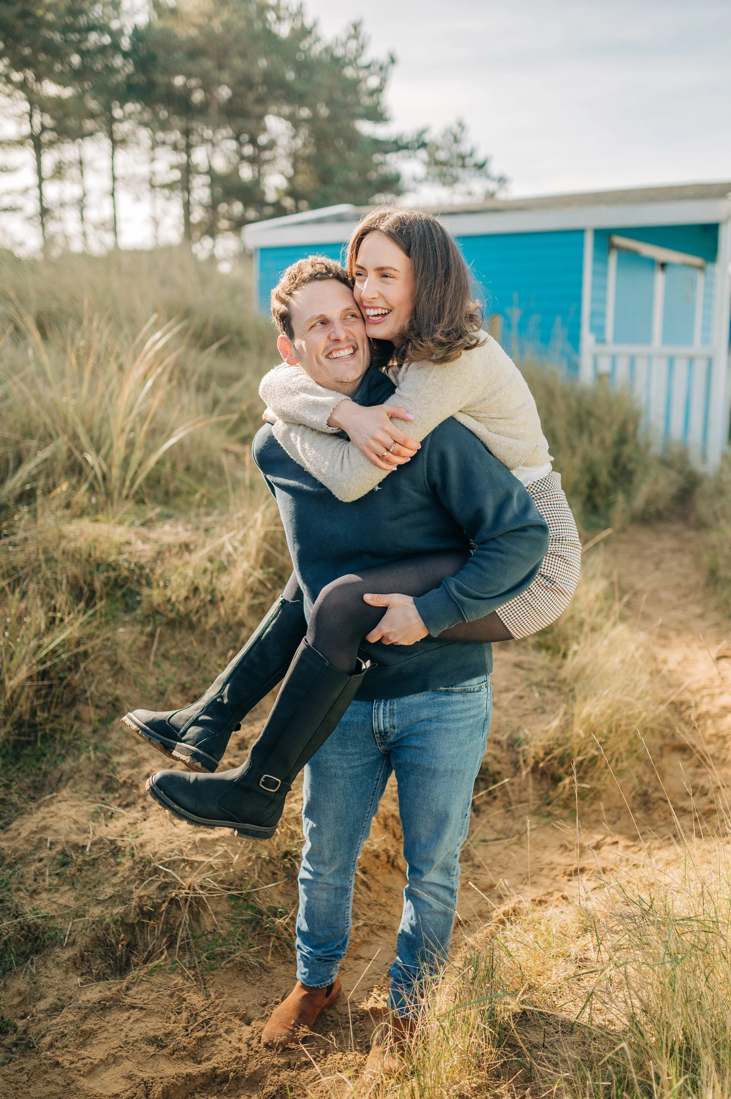 Norfolk Wedding Photographer.  A man holding a woman in an outdoor setting with grass and a blue building in the background.