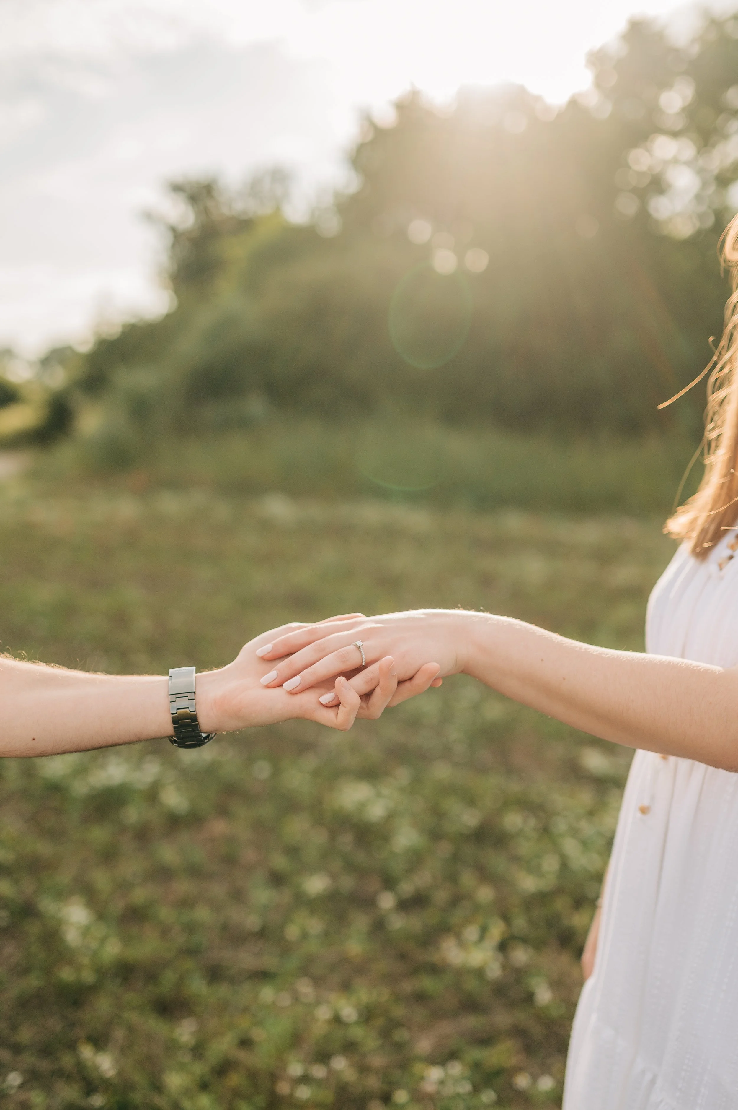 Norfolk Wedding Photographer.  Two women holding hands outdoors at sunset, one woman wearing a wedding ring and a watch, the other woman wearing a white dress.