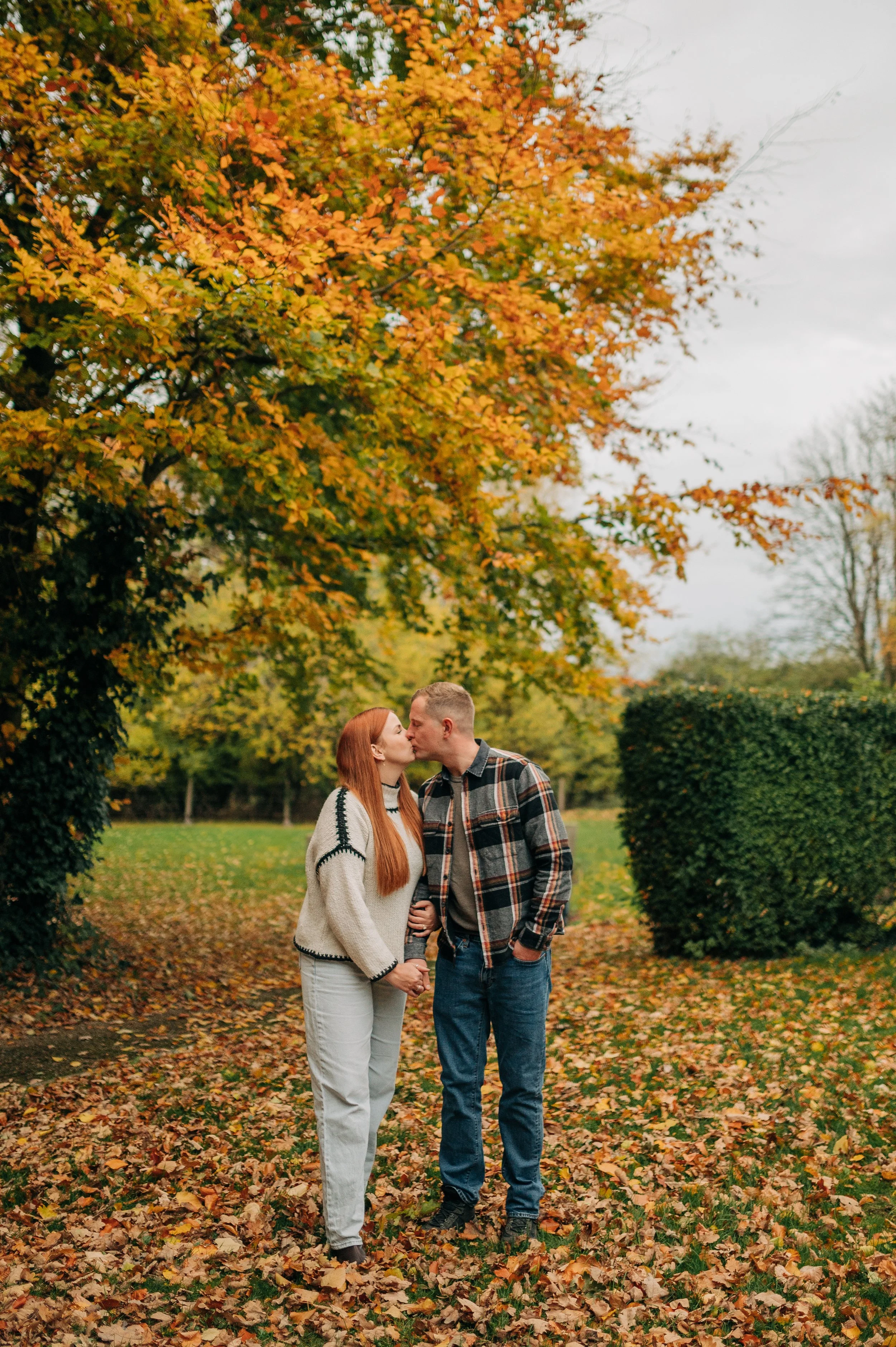 Norfolk Wedding Photographer.  A couple sharing a kiss in a park during autumn with colorful fall foliage.