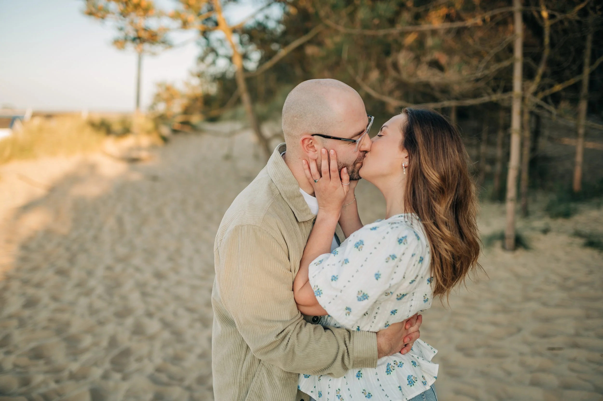 Norfolk Wedding Photographer.  A couple sharing a kiss on a sandy beach with trees in the background during sunset.