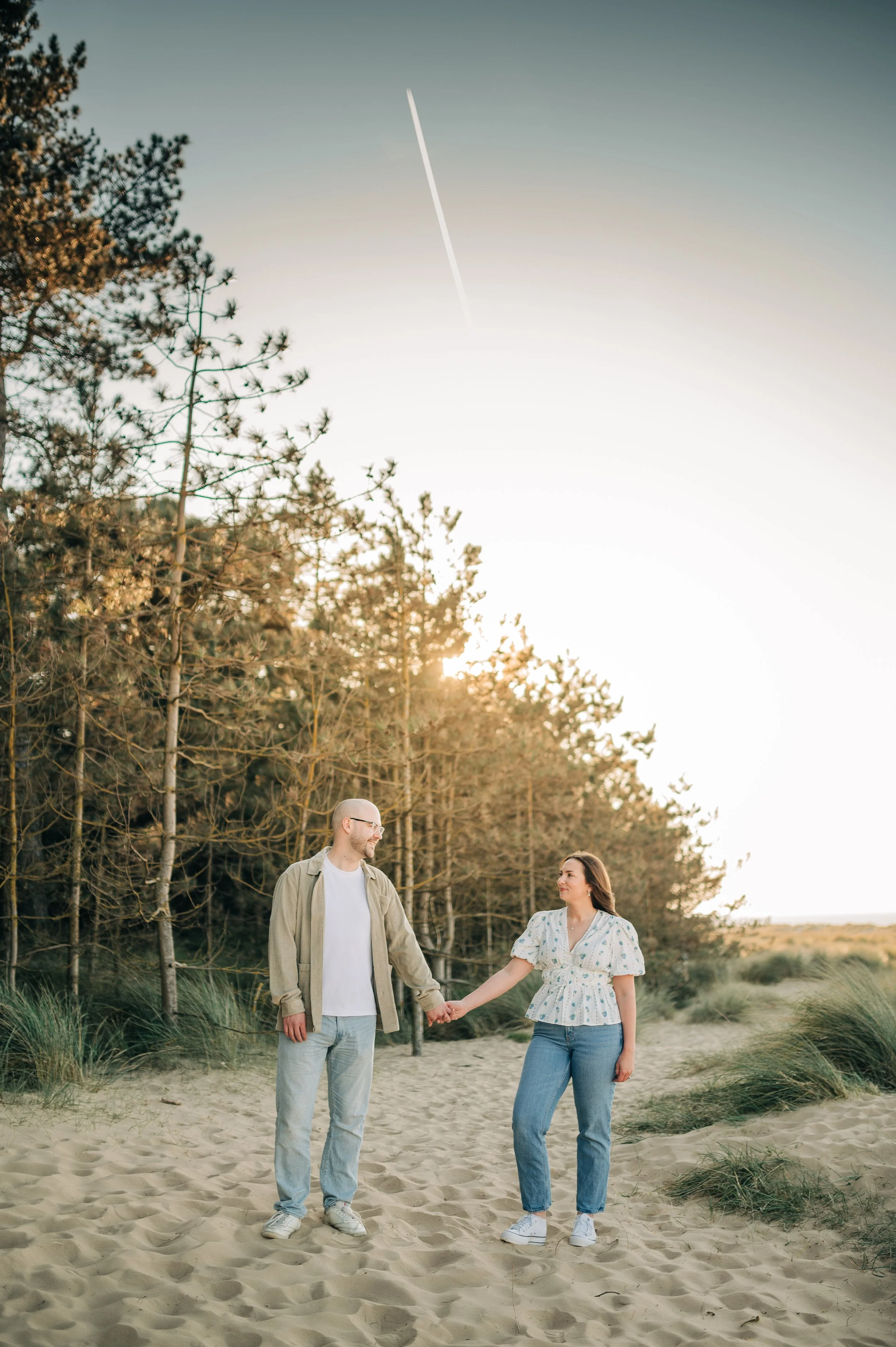 Norfolk Wedding Photographer.  A couple holding hands walking on a sandy beach with trees and grass, during sunset.