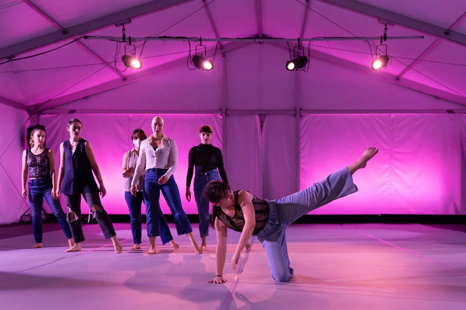 five dancers sway behind soloist hannah lieberman who presses one arm and knee against the ground and extends her other leg in the air