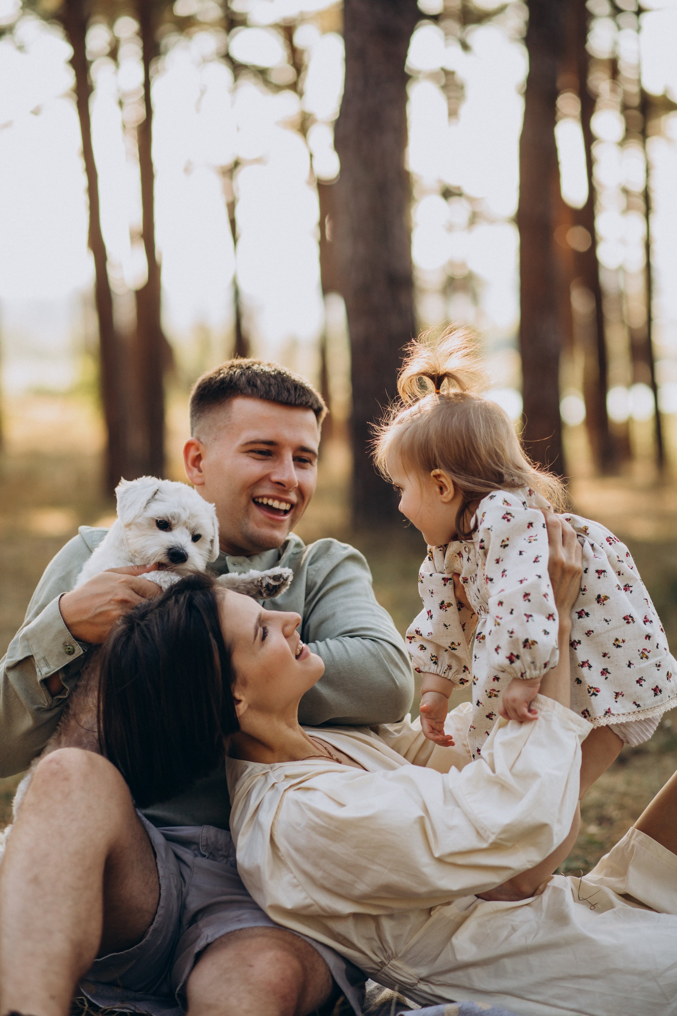 Un groupe de quatre personnes, deux adultes et deux enfants, jouent et s'amusent dans une forêt, avec un petit chien blanc, tous souriants et heureux.