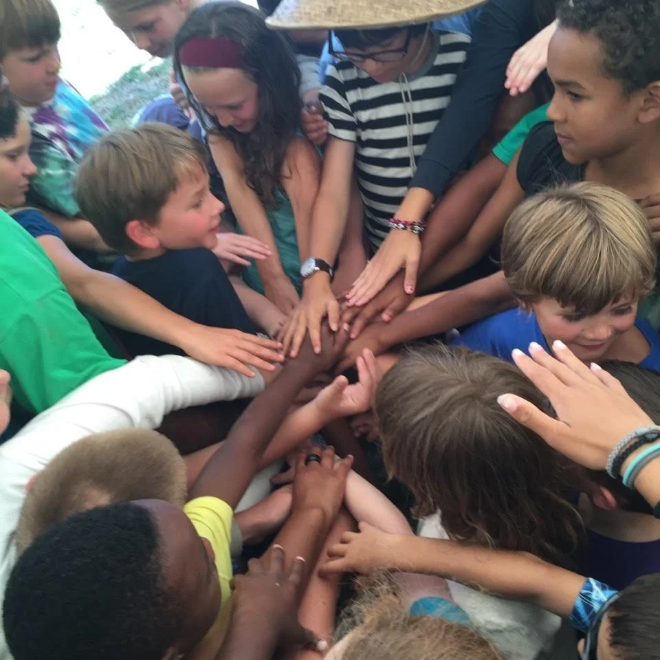 Group of children with hands joined in a circle, symbolizing unity or teamwork.