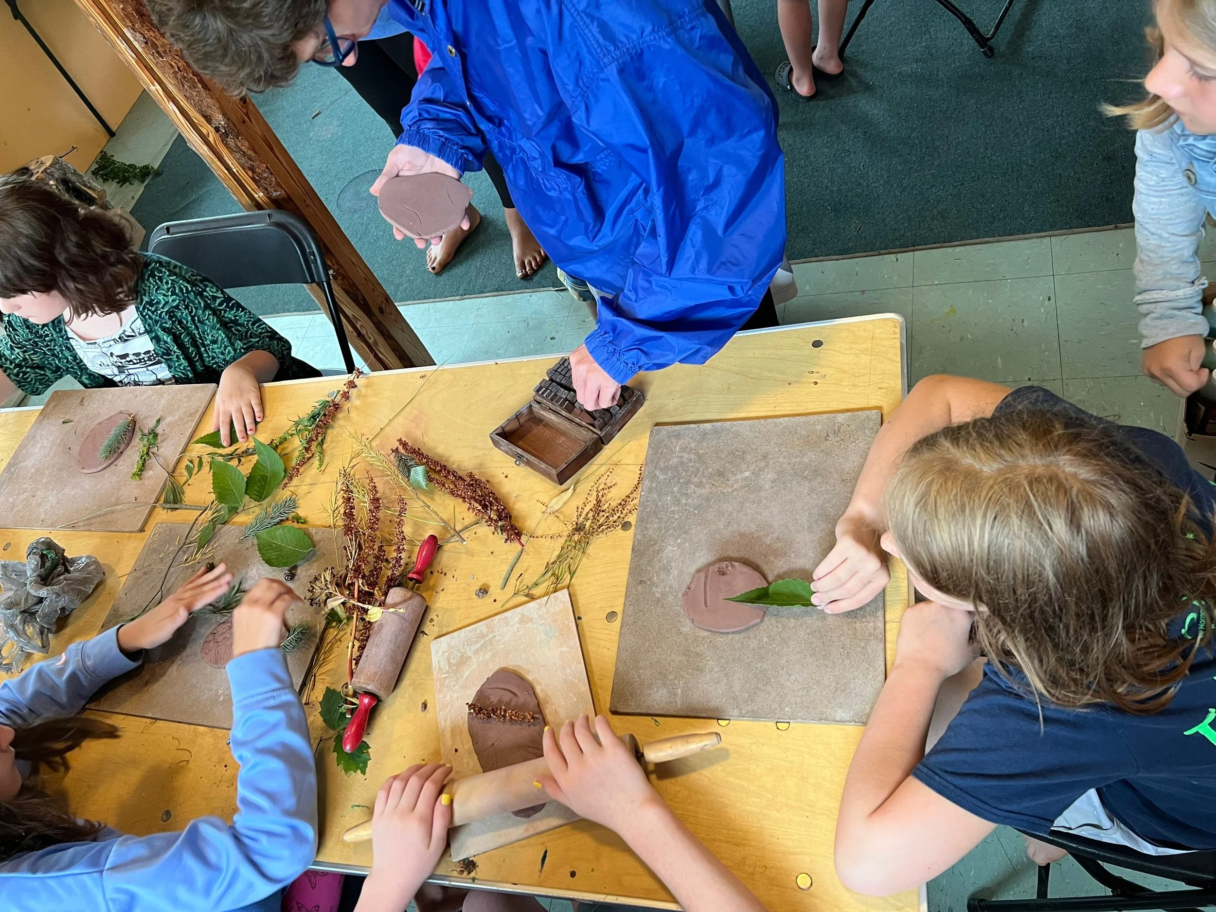 Children creating leaf imprints on clay using natural materials at a table.