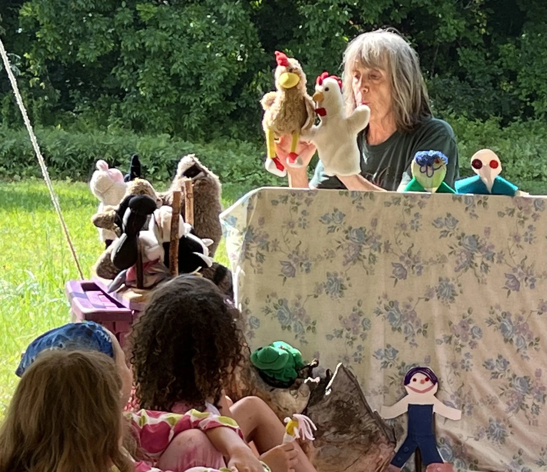 A puppet show being performed outdoors with a person using hand puppets and children watching.
