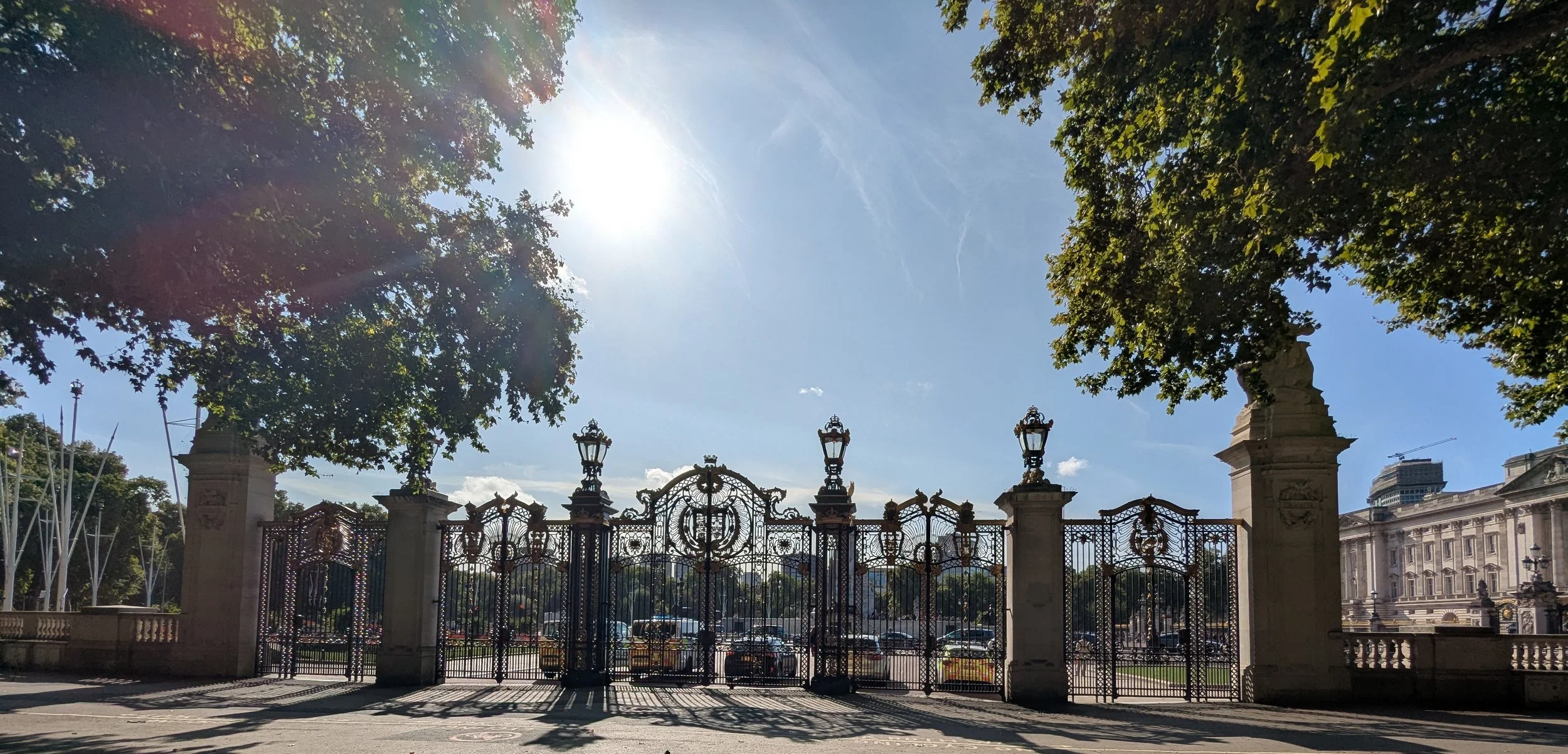 Outside Buckingham Palace, Ornate wrought-iron fence with lanterns, trees, sunshine