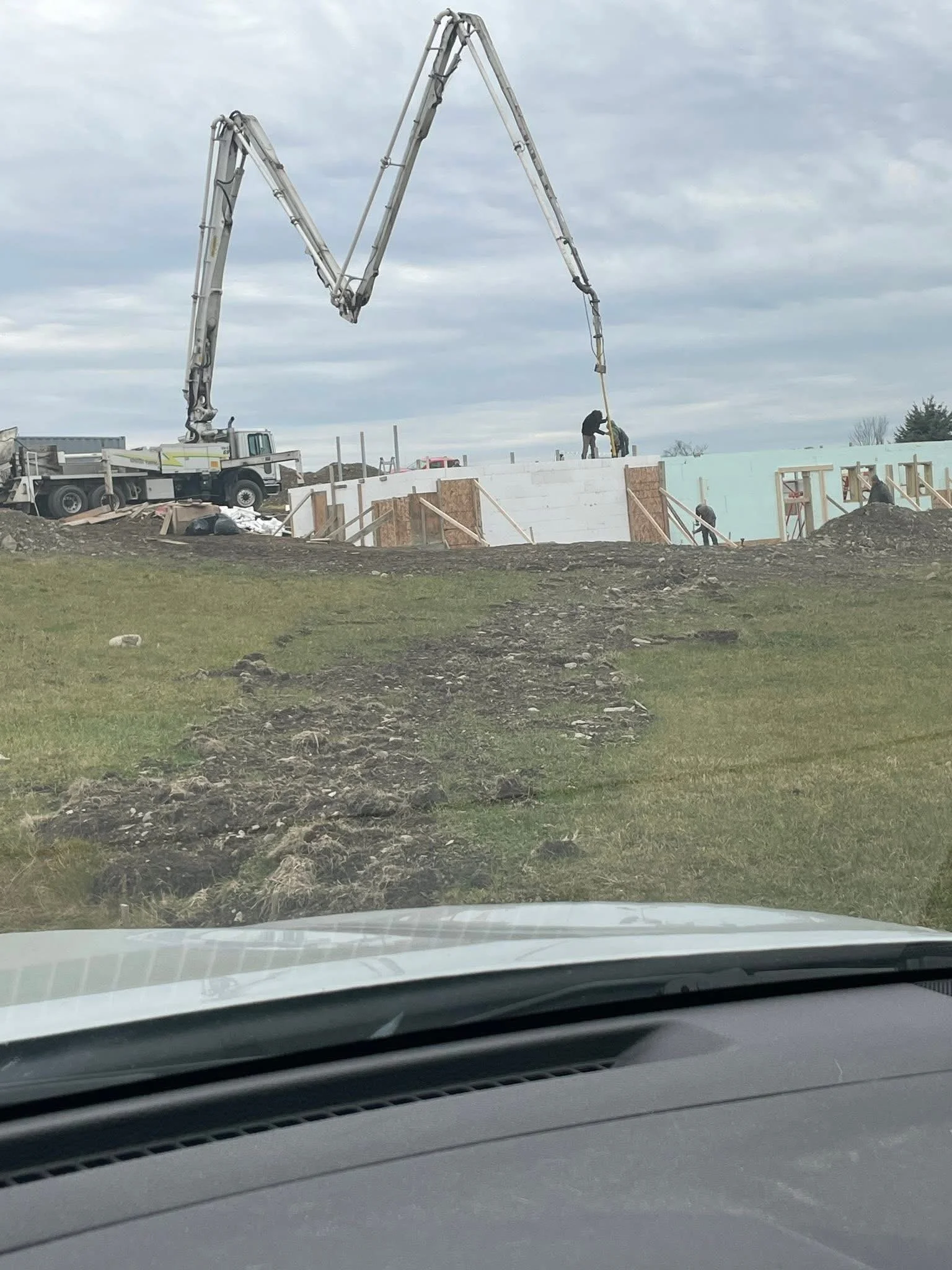 Construction workers building a large concrete structure outdoors, with a boom pump truck pouring concrete, and visible construction materials and tools around.