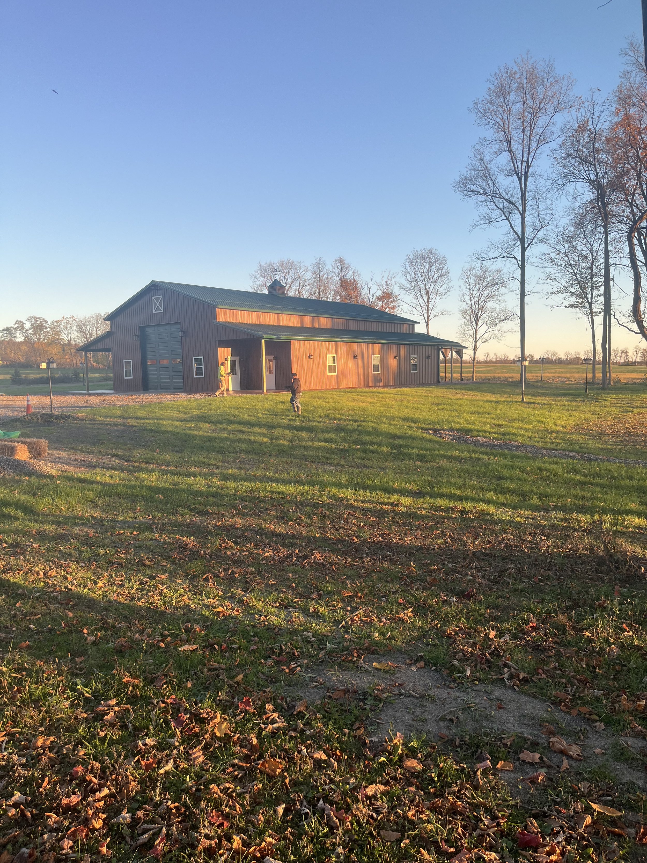 A rural barn with a metal roof and new windows, illuminated by late afternoon sunlight, with leafless trees and open fields in the background.