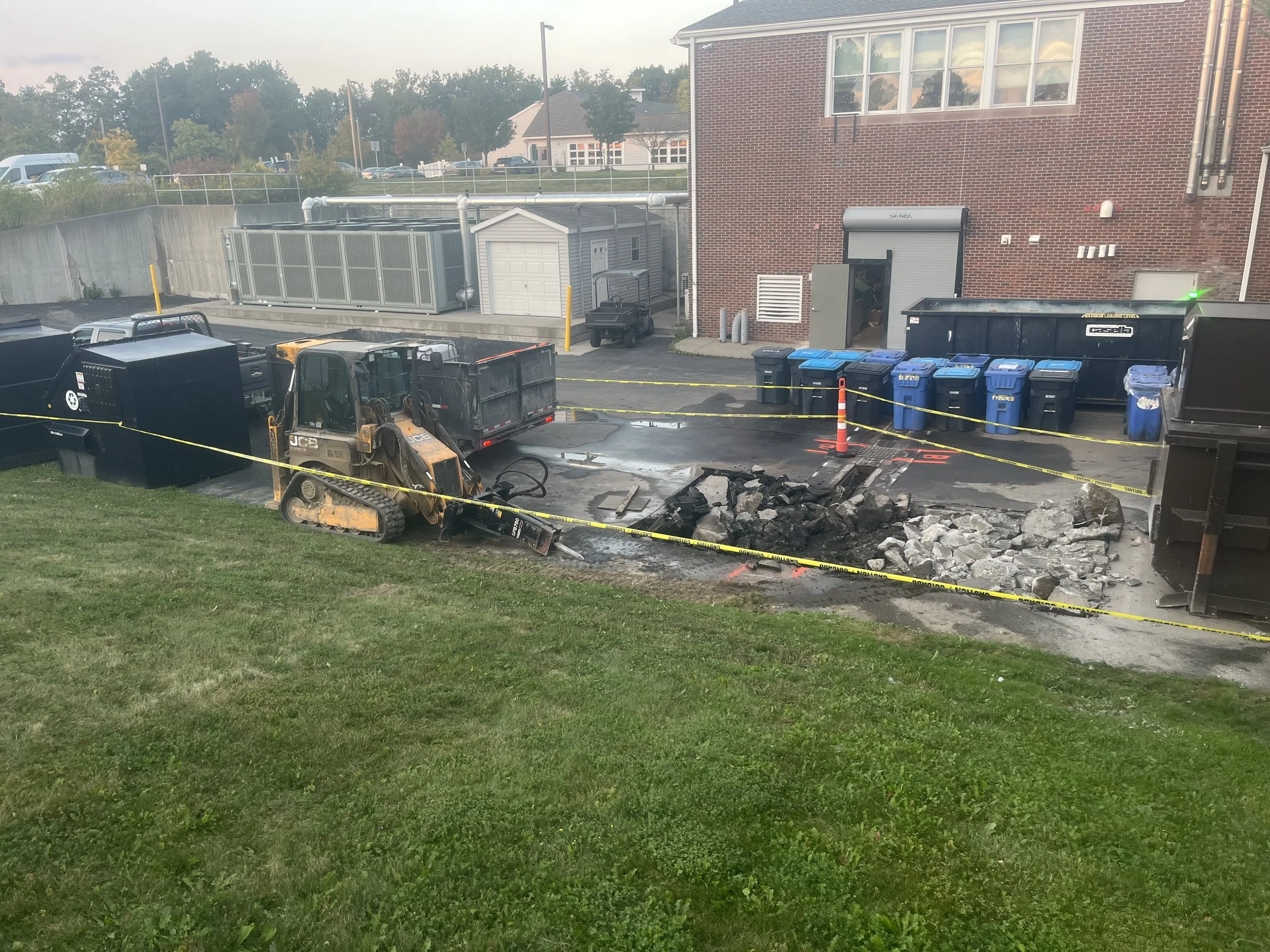 Construction area with a bulldozer, debris, yellow caution tape, and dumpsters near a brick building