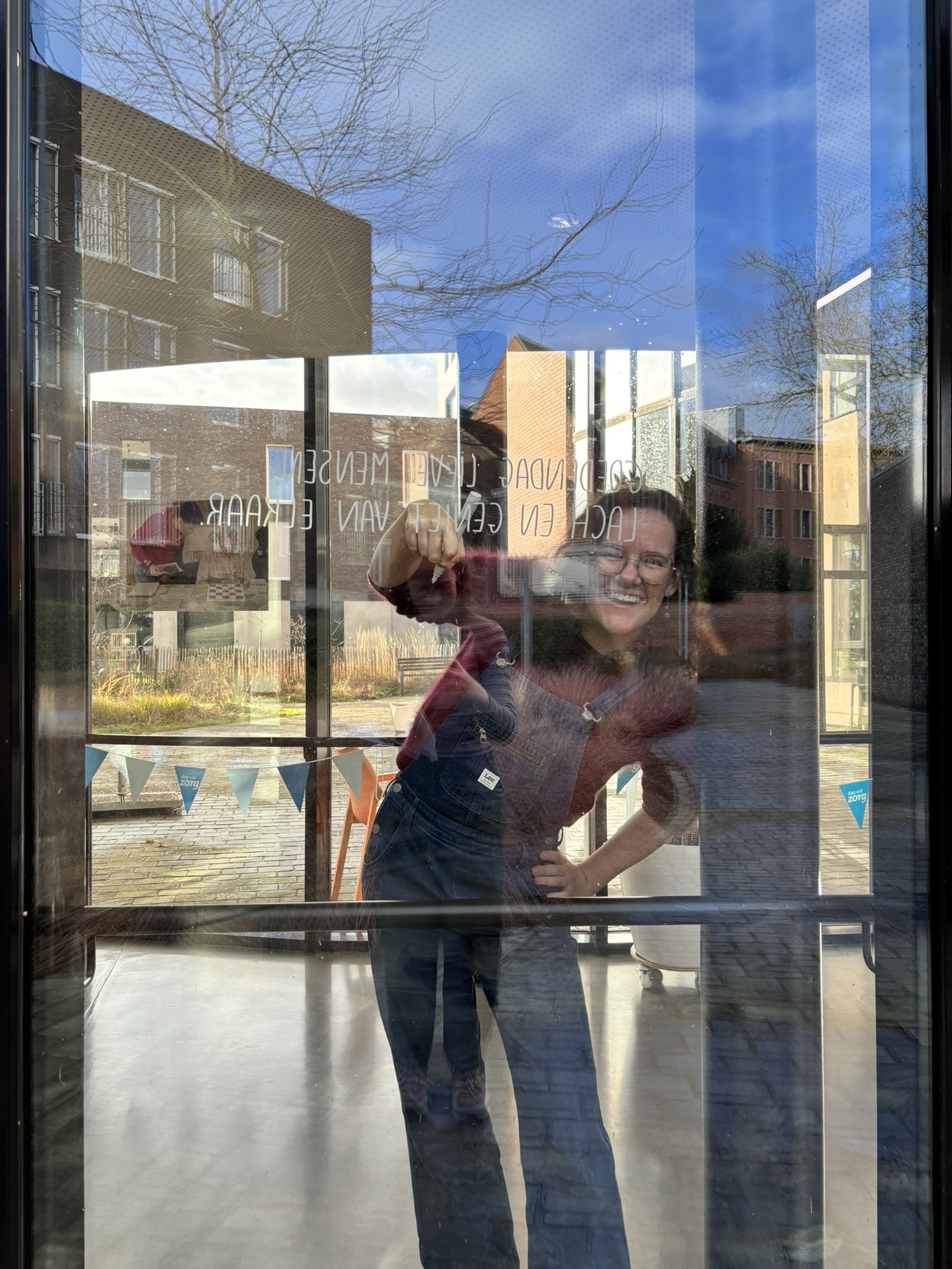 A person looks through a glass door with reflections of a building and a tree.