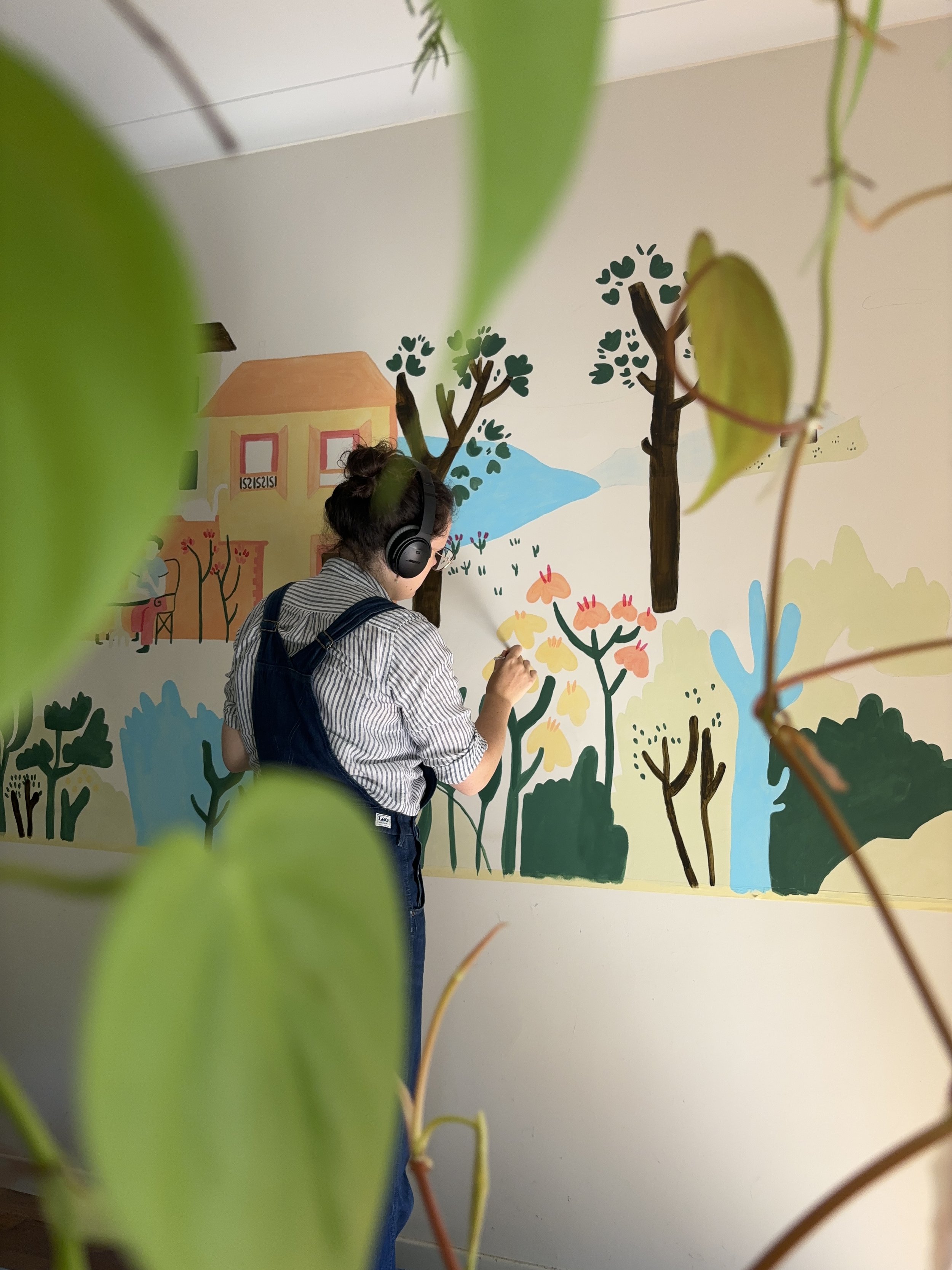 Aurelie paints a colorful mural of trees and flowers, with plants in the foreground.