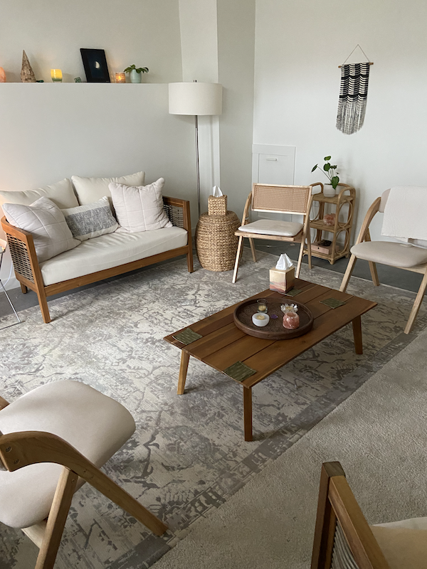 neutral-colored chairs and loveseat around a wooden slat coffee table holding a tray, candles, and tissue box