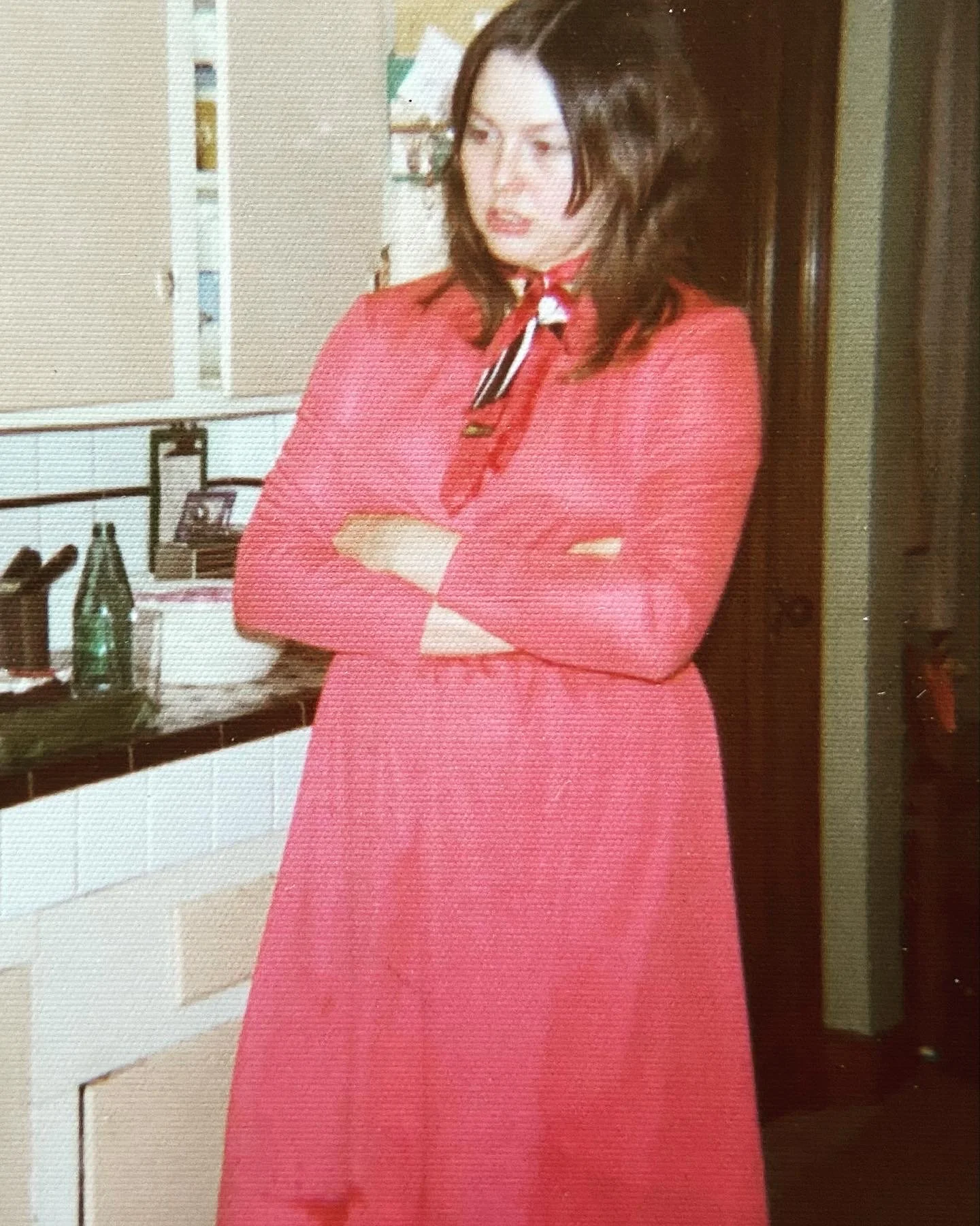 White woman with dark hair in a red dress and a red scarf with her arms crossed