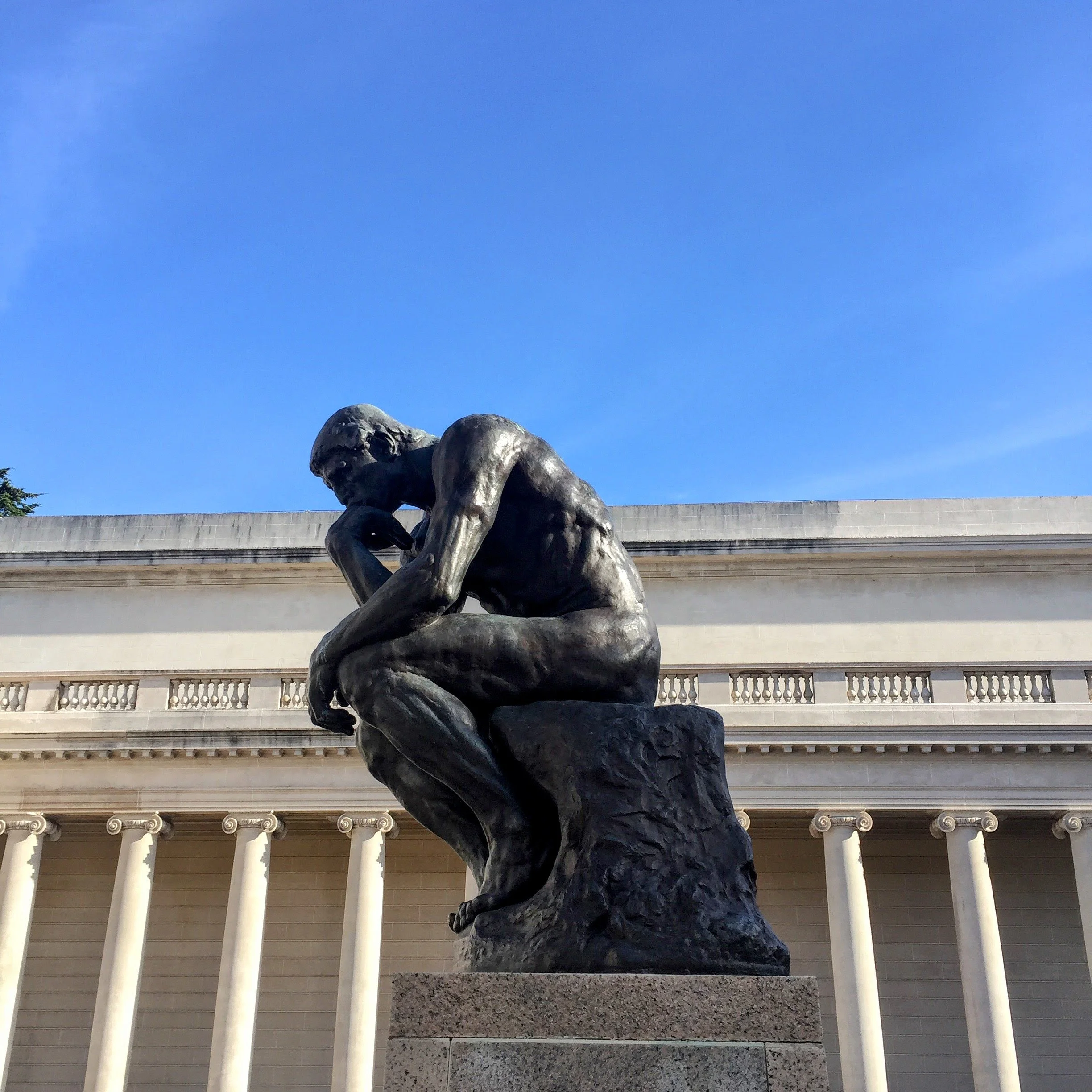 Rodin's The Thinker sculpture in front of columned building and blue sky