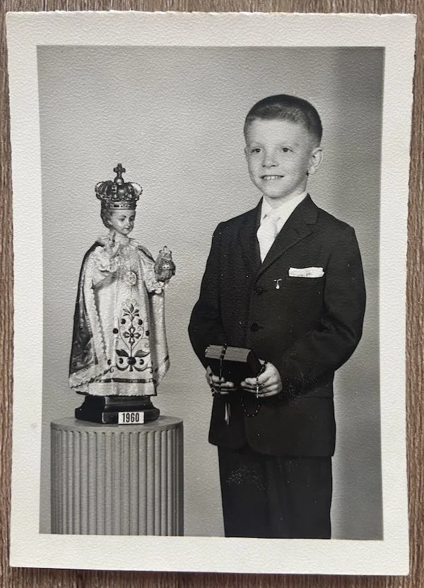 Tamara's dad when he was young holding a bible and rosary, and standing next to a statue of child Jesus.