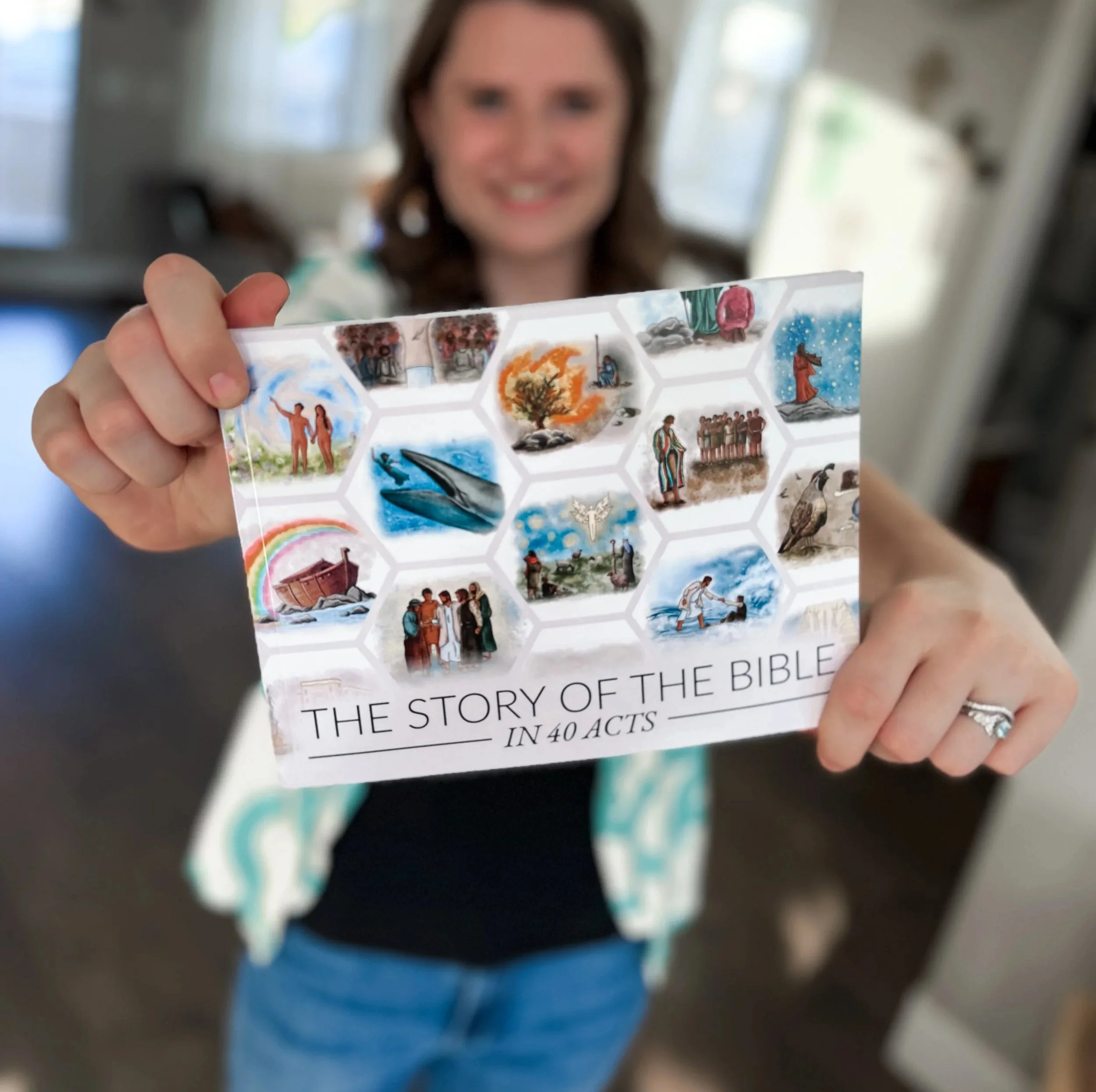 Berlynn Burns from The Burns Creative holding a booklet titled "The Story of the Bible in 40 Acts" with various scripture illustrations on the cover, including a whale, rainbow, people, and religious scenes.