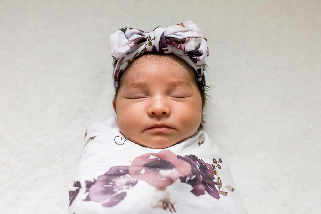 Close-up of a newborn baby wrapped in a floral blanket and wearing a matching headband, sleeping peacefully.