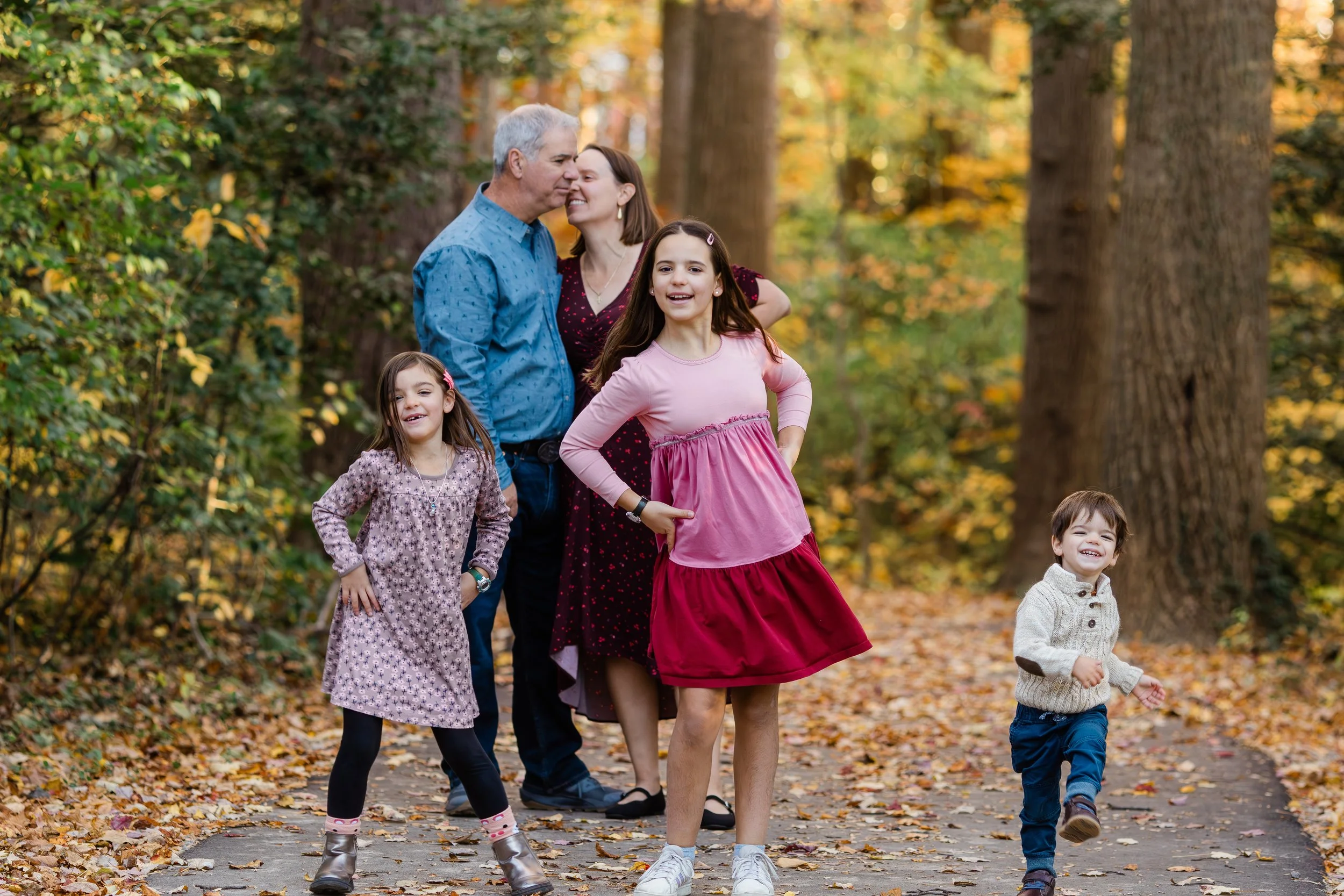 Family of five with two adults and three children walking through a fall forest with colorful autumn leaves, laughing and enjoying a day outdoors.