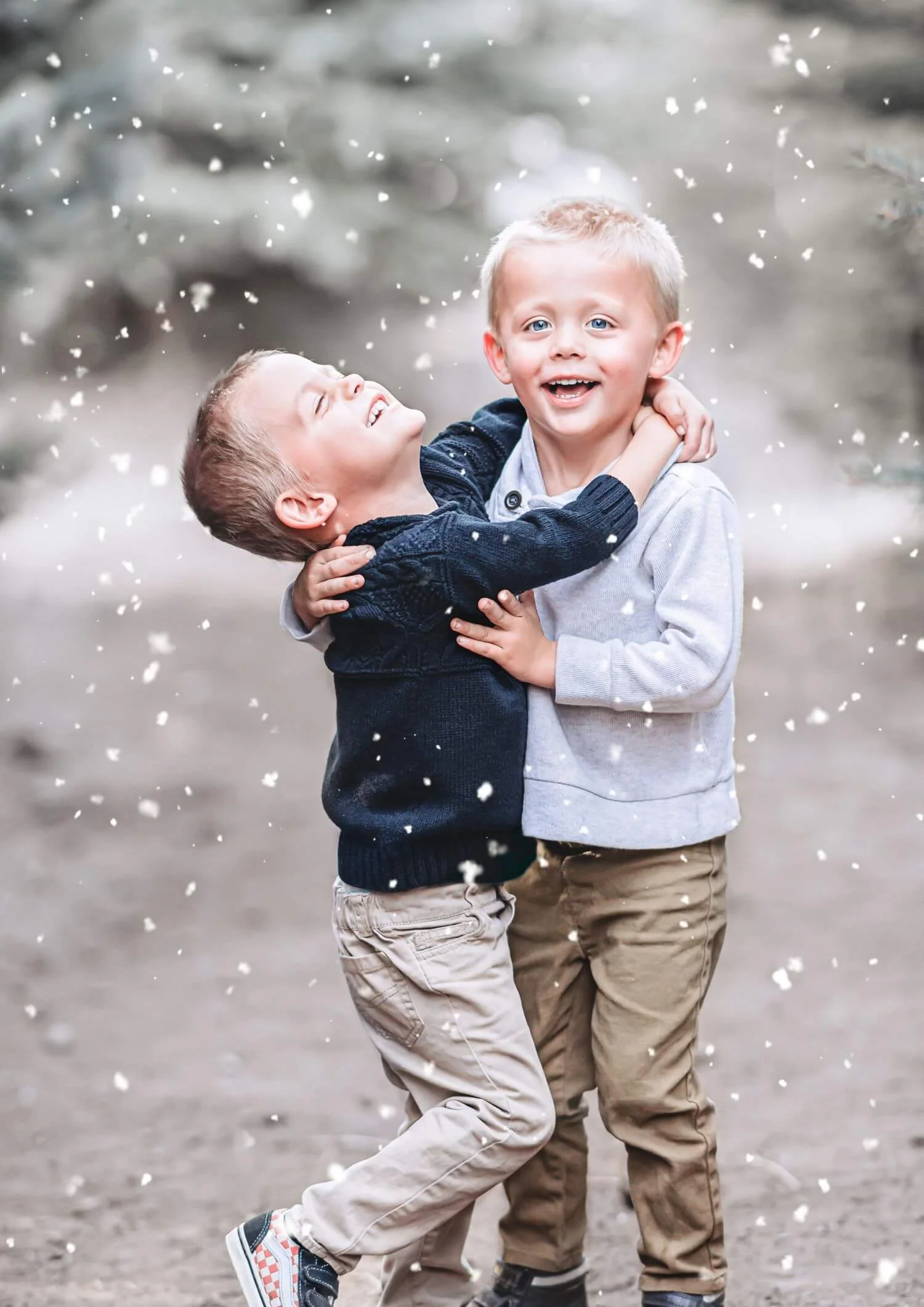 Two young boys with blond hair and blue eyes happily playing and hugging each other outside in the snow.