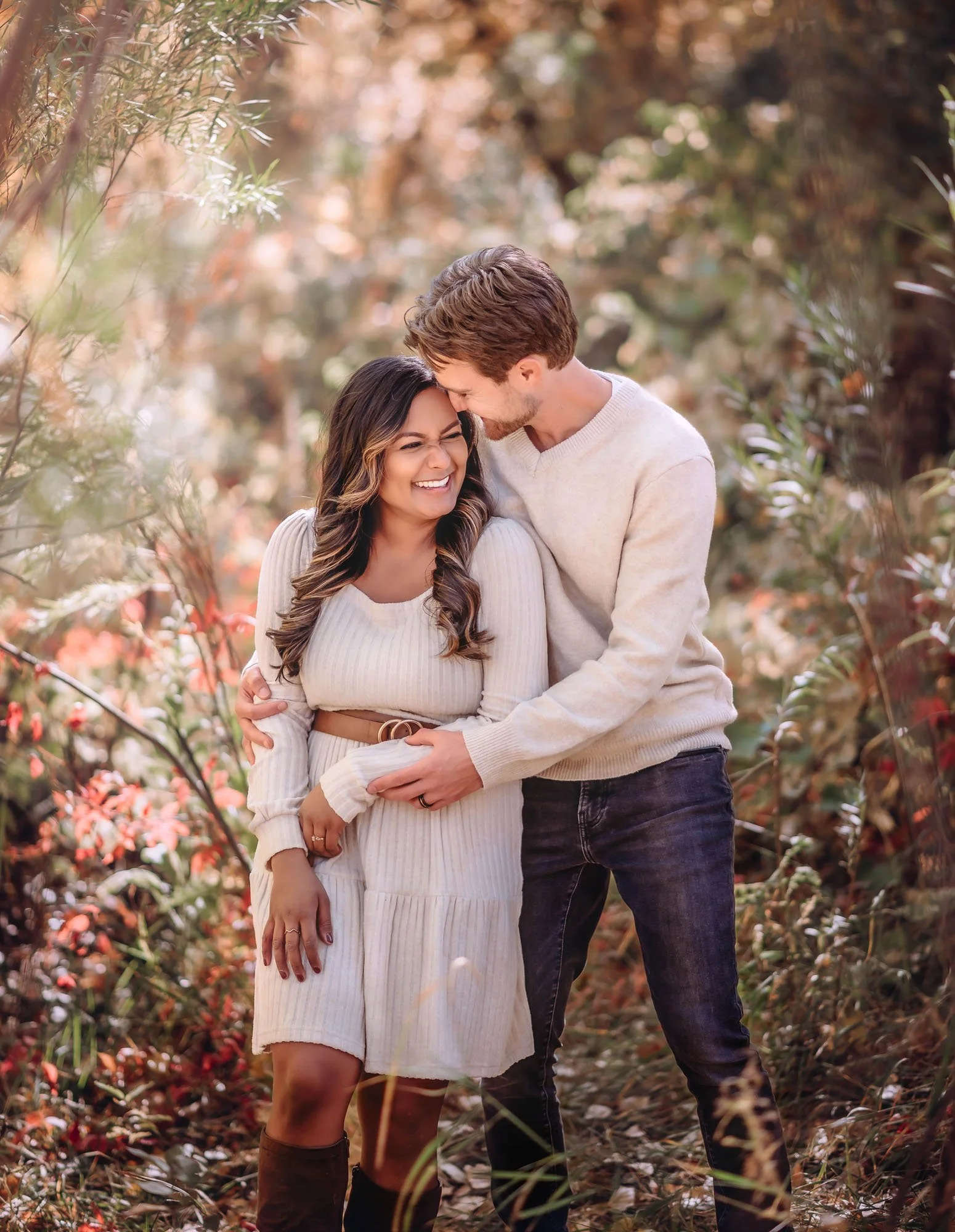 A happy couple hugs in a park during autumn, surrounded by fall foliage.