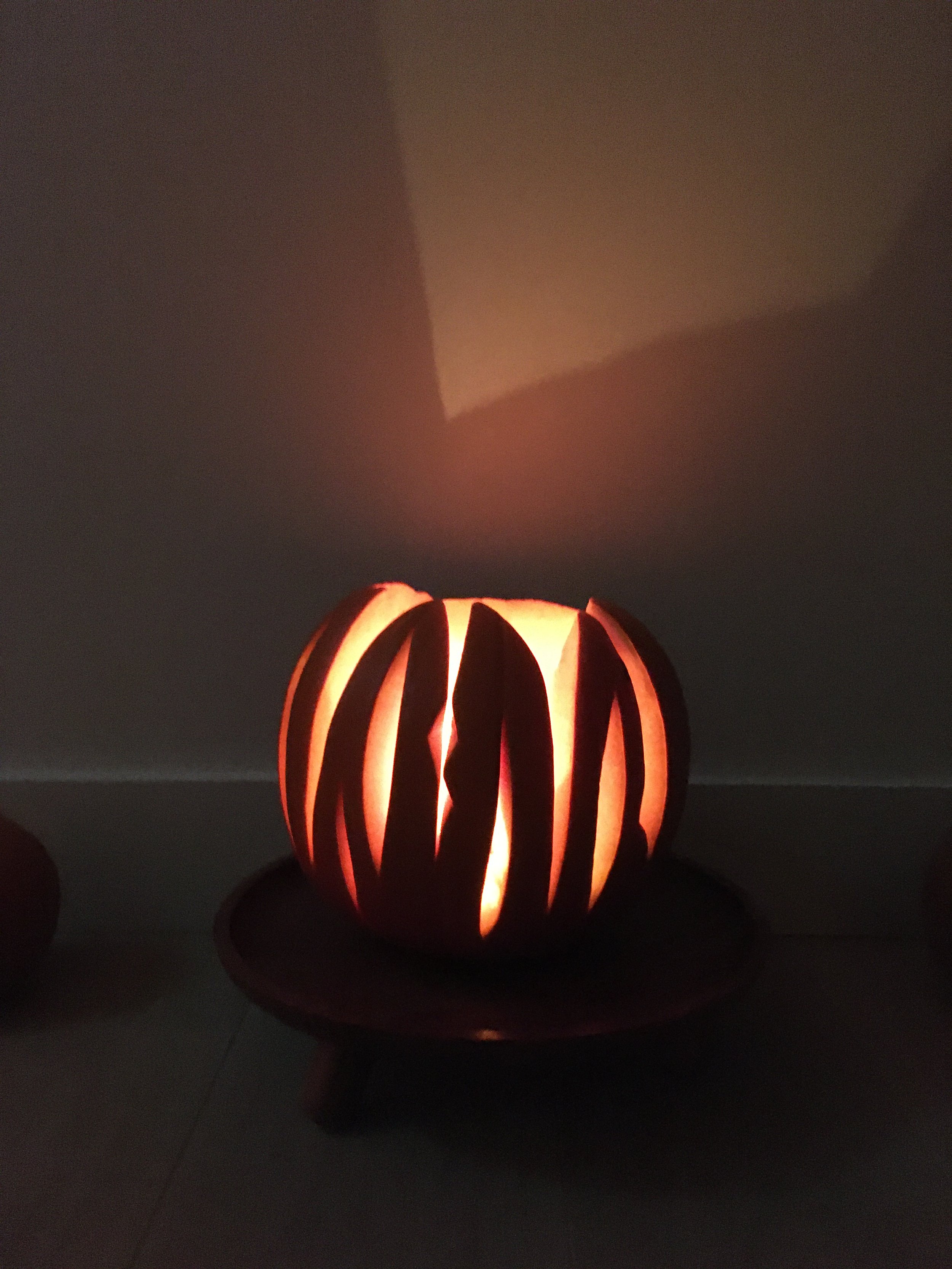 A photo of a carved pumpkin in the dark. It has big slabs cut away so it looks sharp, agressive, and intriguing. Inside it is illuminated.