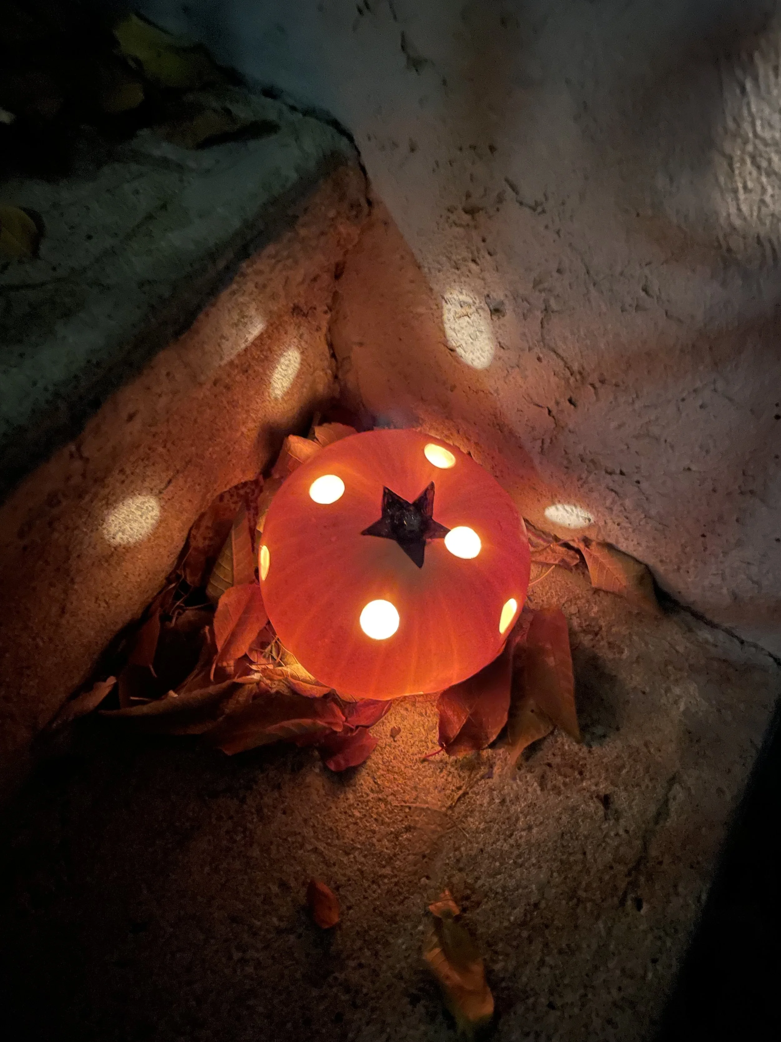 A photo of a carved pumpkin in the dark. Inside it is illuminated. Shot from above it shoes a pumpkin with evenly space holes, the same size, and a black star painted at the case of the stem. 