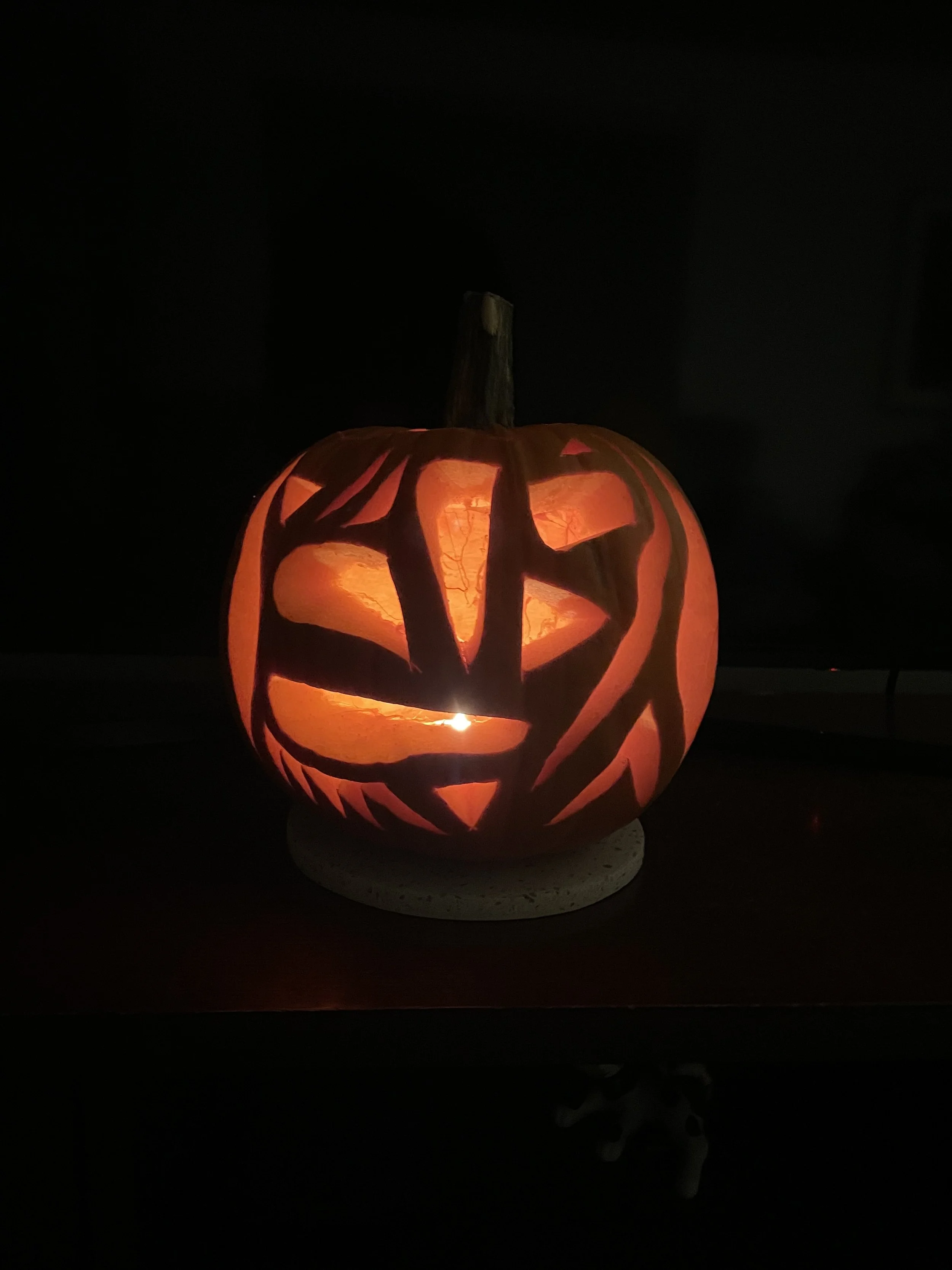 A photo of a carved pumpkin in the dark. Inside it is illuminated. It appears like a puzzle or a map. With big chunks missing and thick lines.