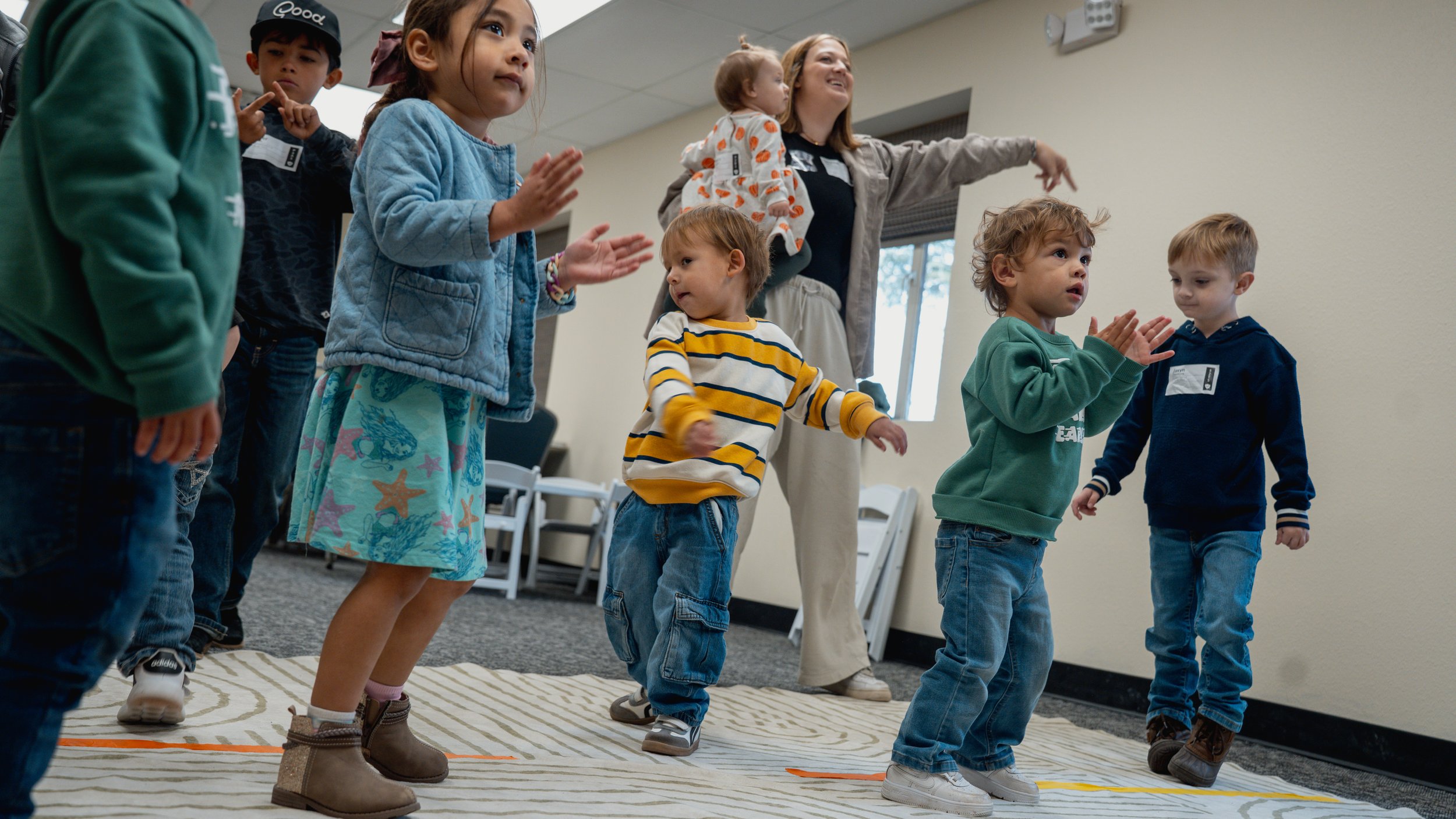 Children participating in a group activity inside a classroom, led by a female instructor.