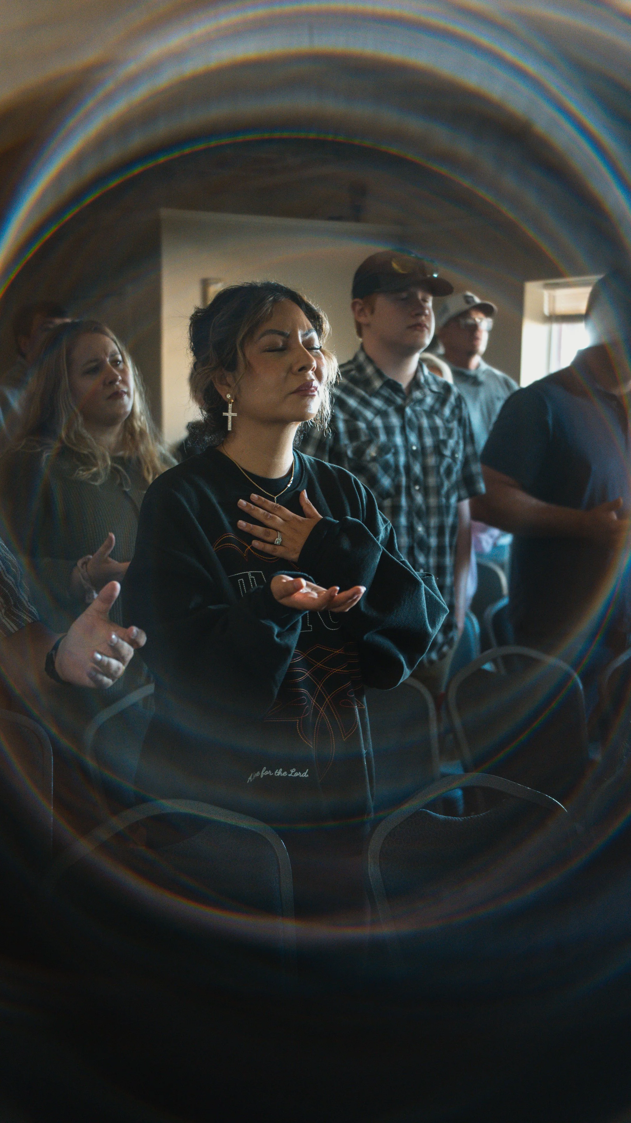 People praying or worshiping during a religious service, with their hands raised or clasped, seen through a circular stained glass window.