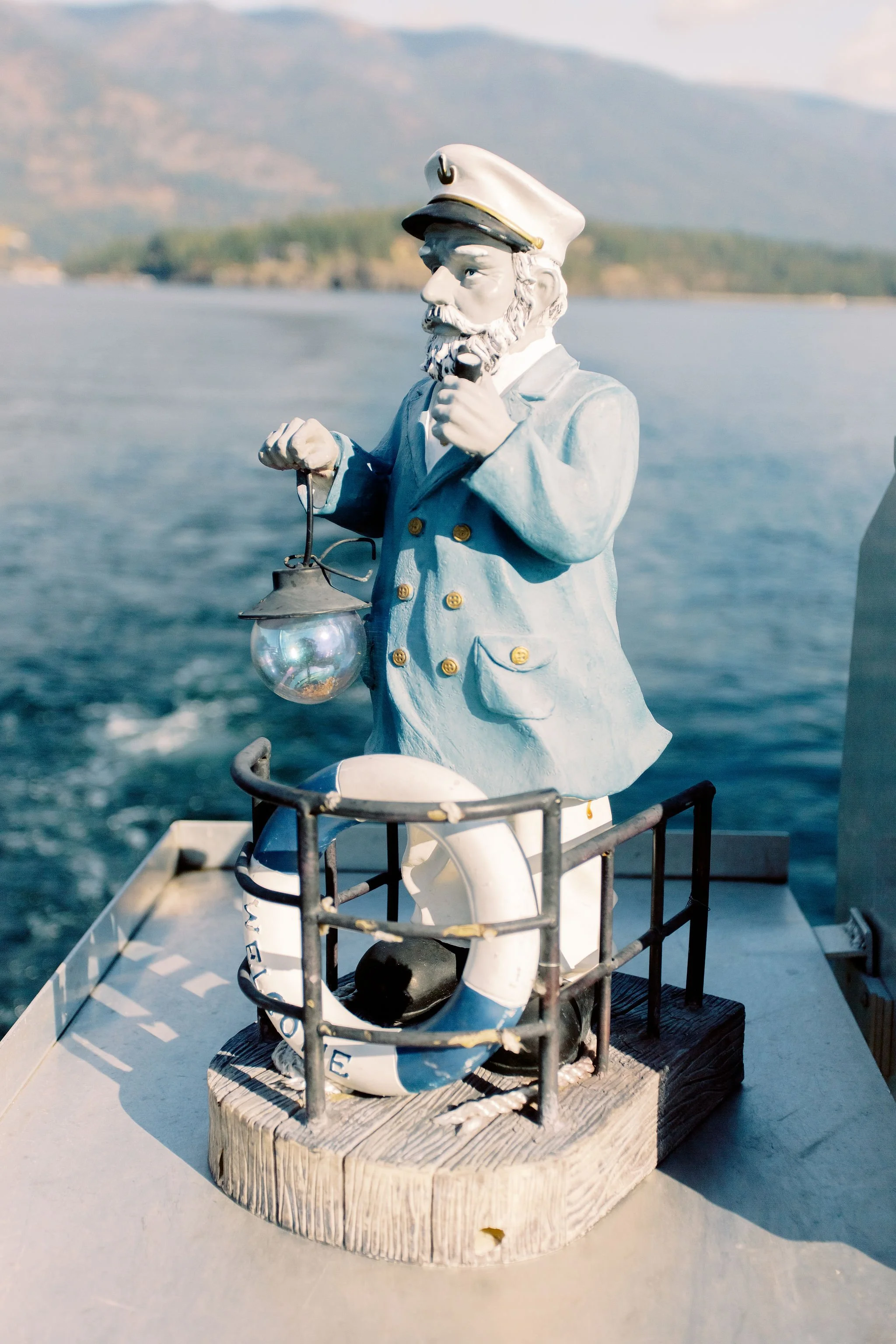 Decorative lighthouse figurine of a captain on a boat with a scenic water and mountain background