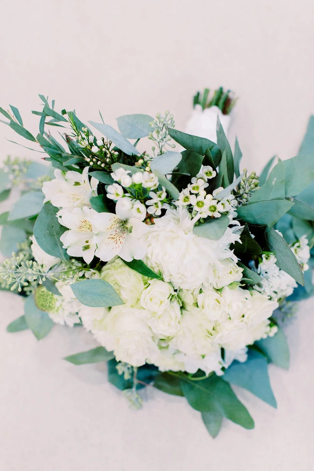 Close-up of a white floral bouquet with greenery, including leaves and small white flowers.