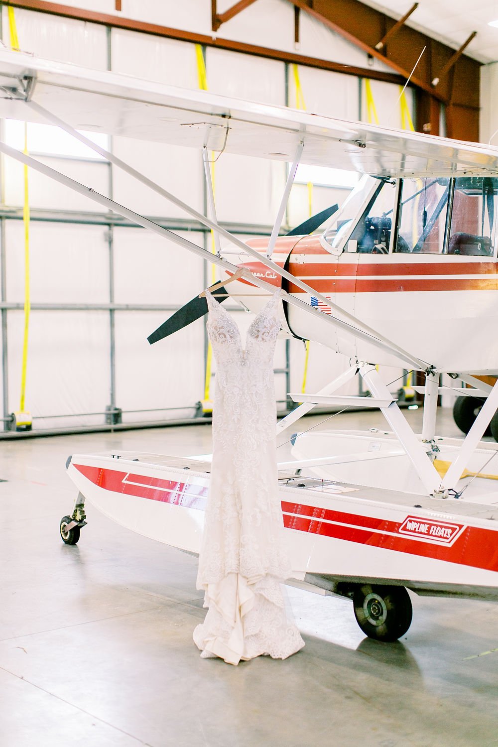 A wedding dress hanging from a prop lift on a small airplane inside a hangar.