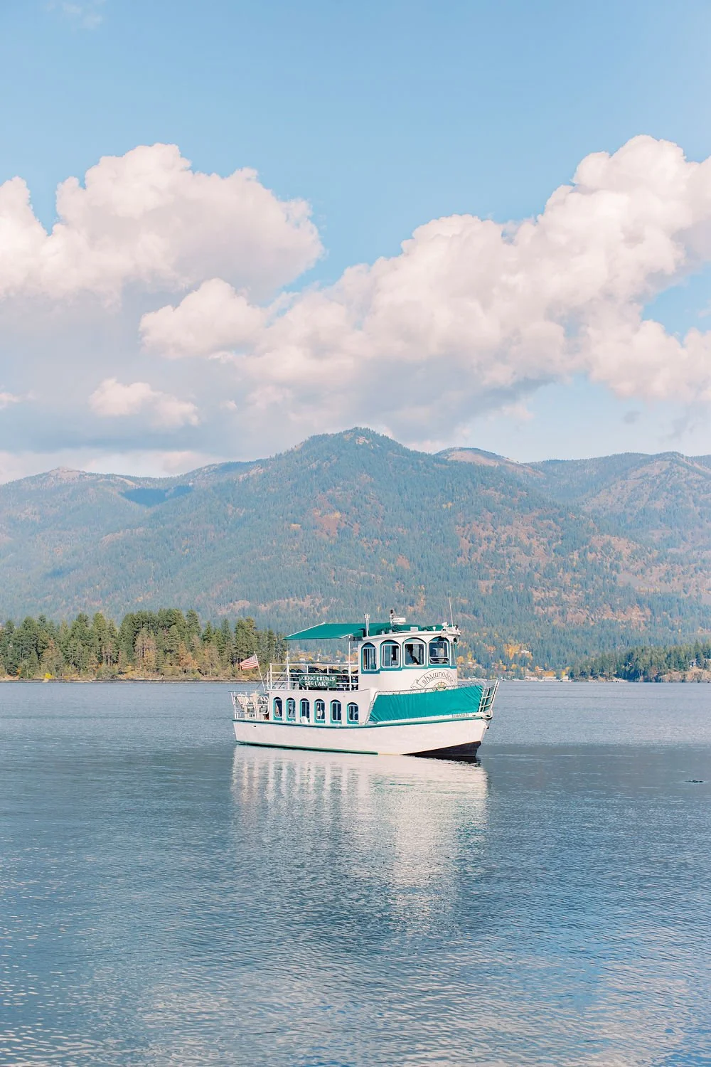 A boat on a calm lake with mountains and partly cloudy sky in the background.