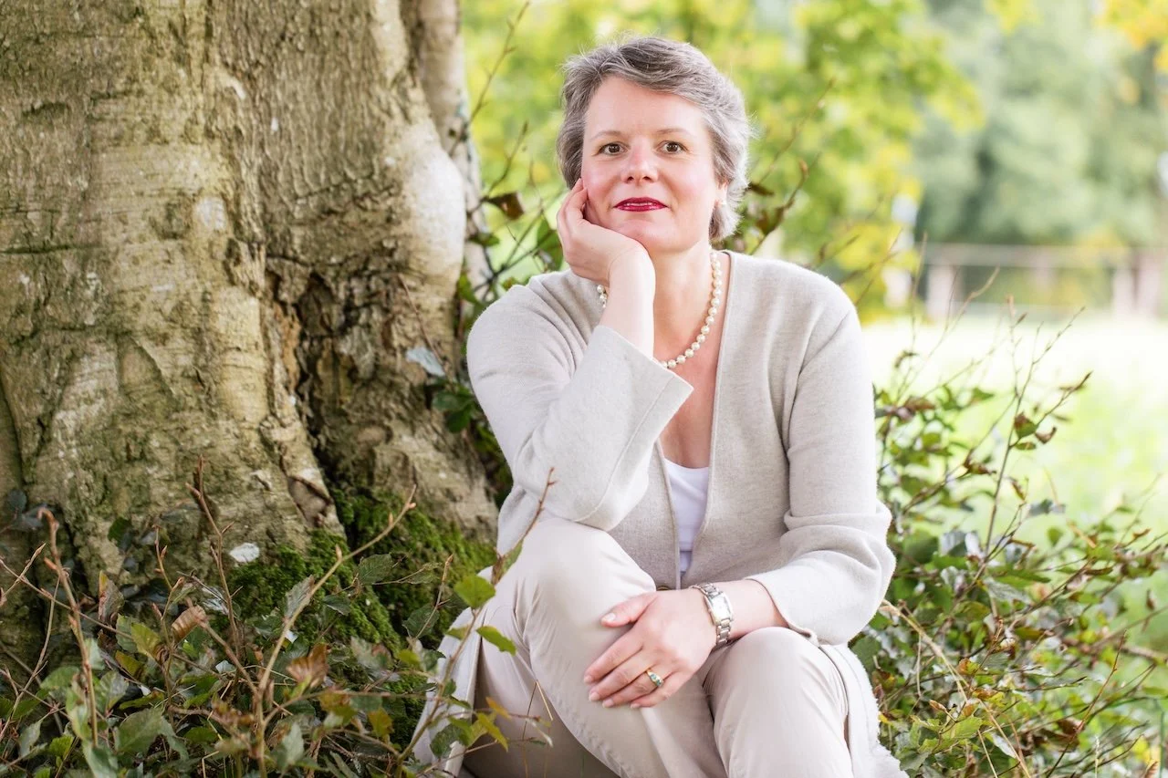 Lydia Böhm, Bankerin und Hamburgerin, im nachdenklichen Porträt vor alter Baumrinde, Hand am Kinn, Blick zur Betrachterin.