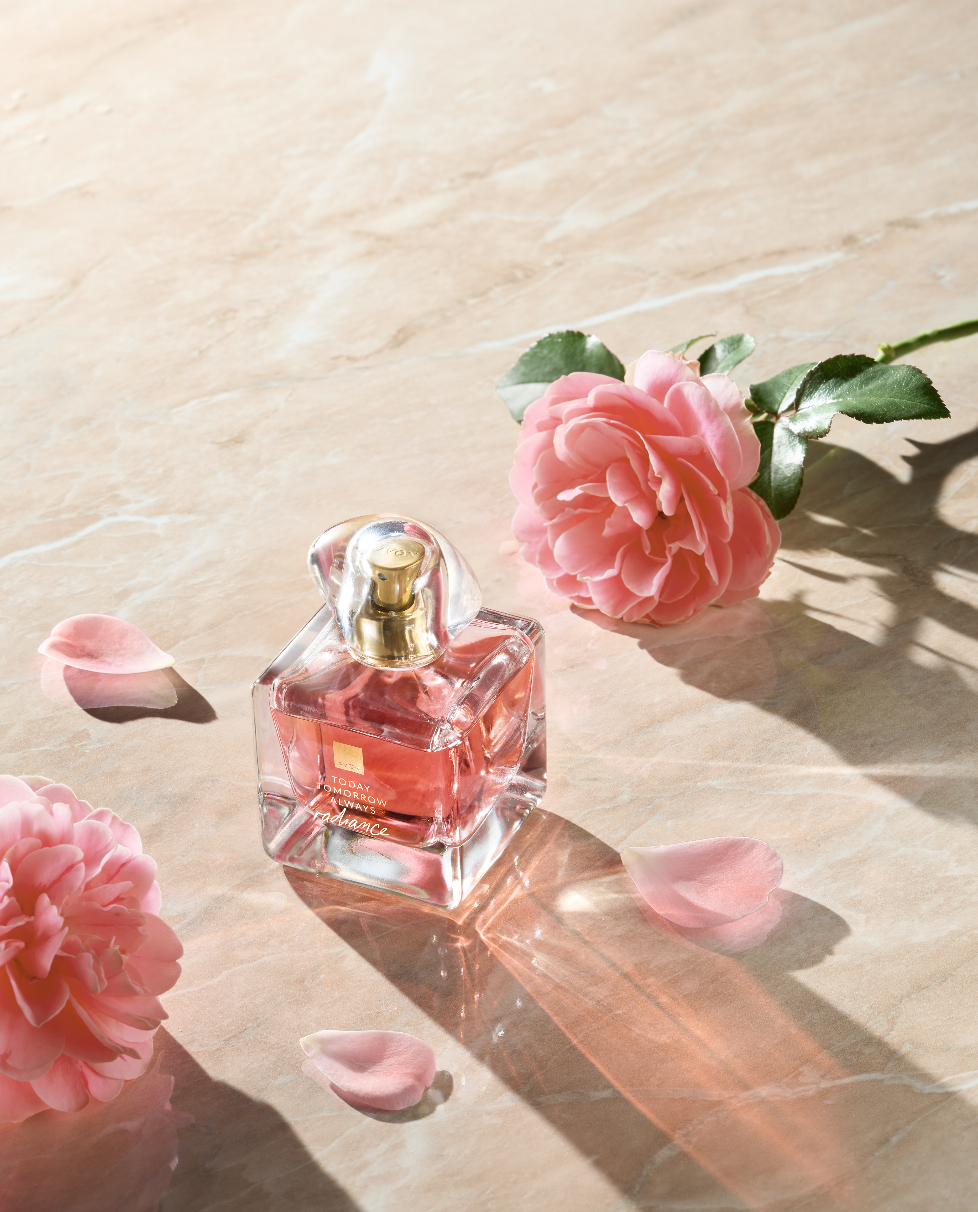 Avon fragrance bottle surrounded by pink flowers and petals, styled in soft natural light.