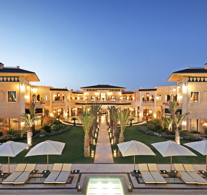 Evening view of Palais Ronsard Relais & Châteaux with illuminated courtyard, palm-lined gardens and swimming pool.