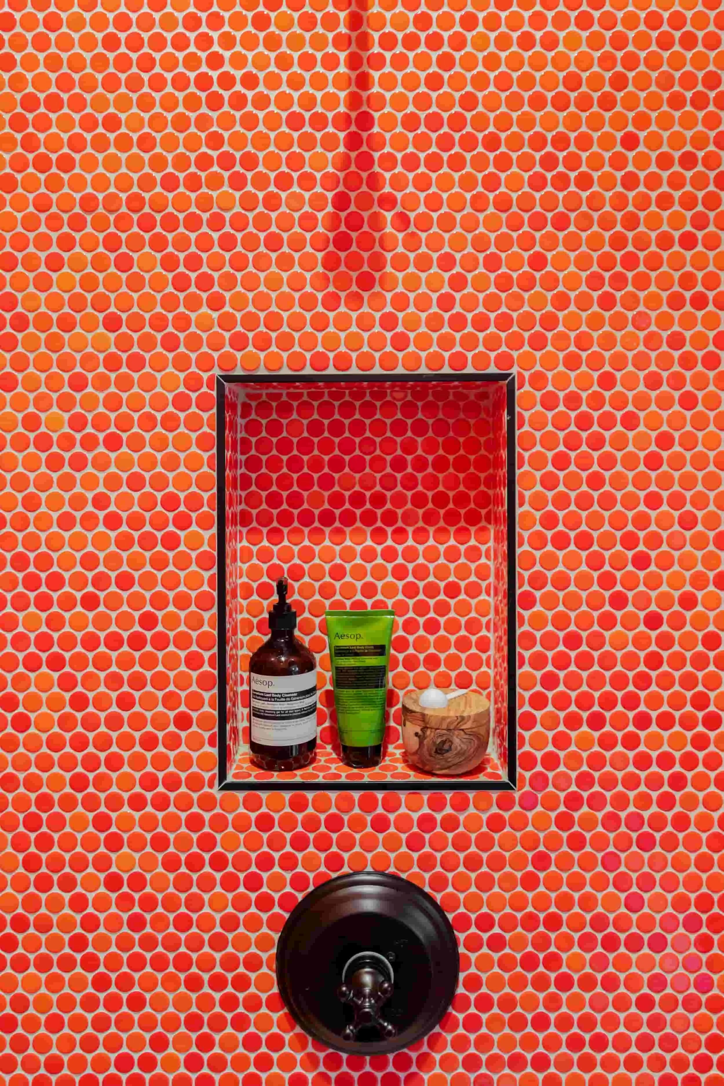 Bright orange penny tile shower with a recessed niche holding body care products above a dark bronze shower valve.