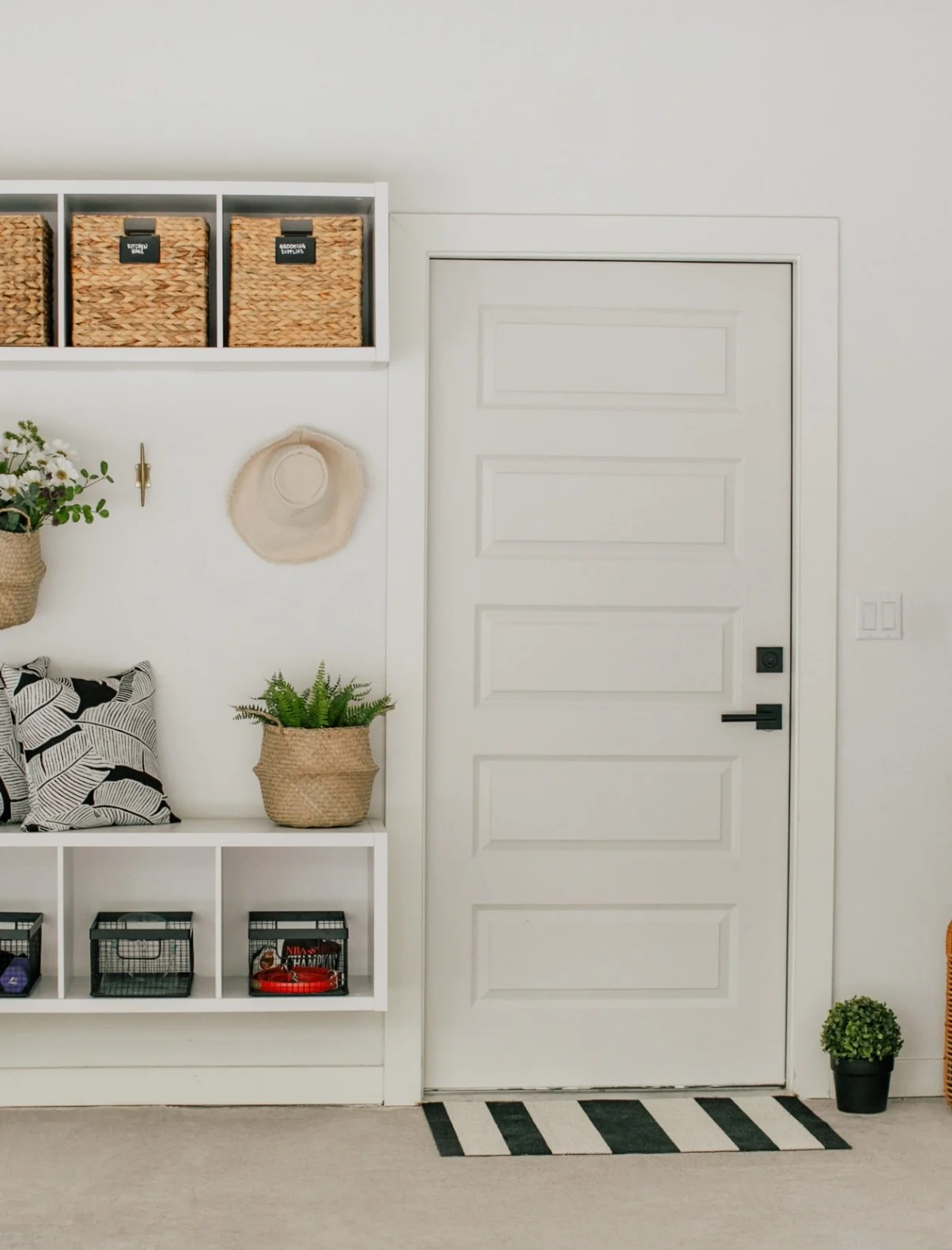 Garage organized by Hannah Goetz with white built-in storage, woven baskets, a bench, and a striped rug.