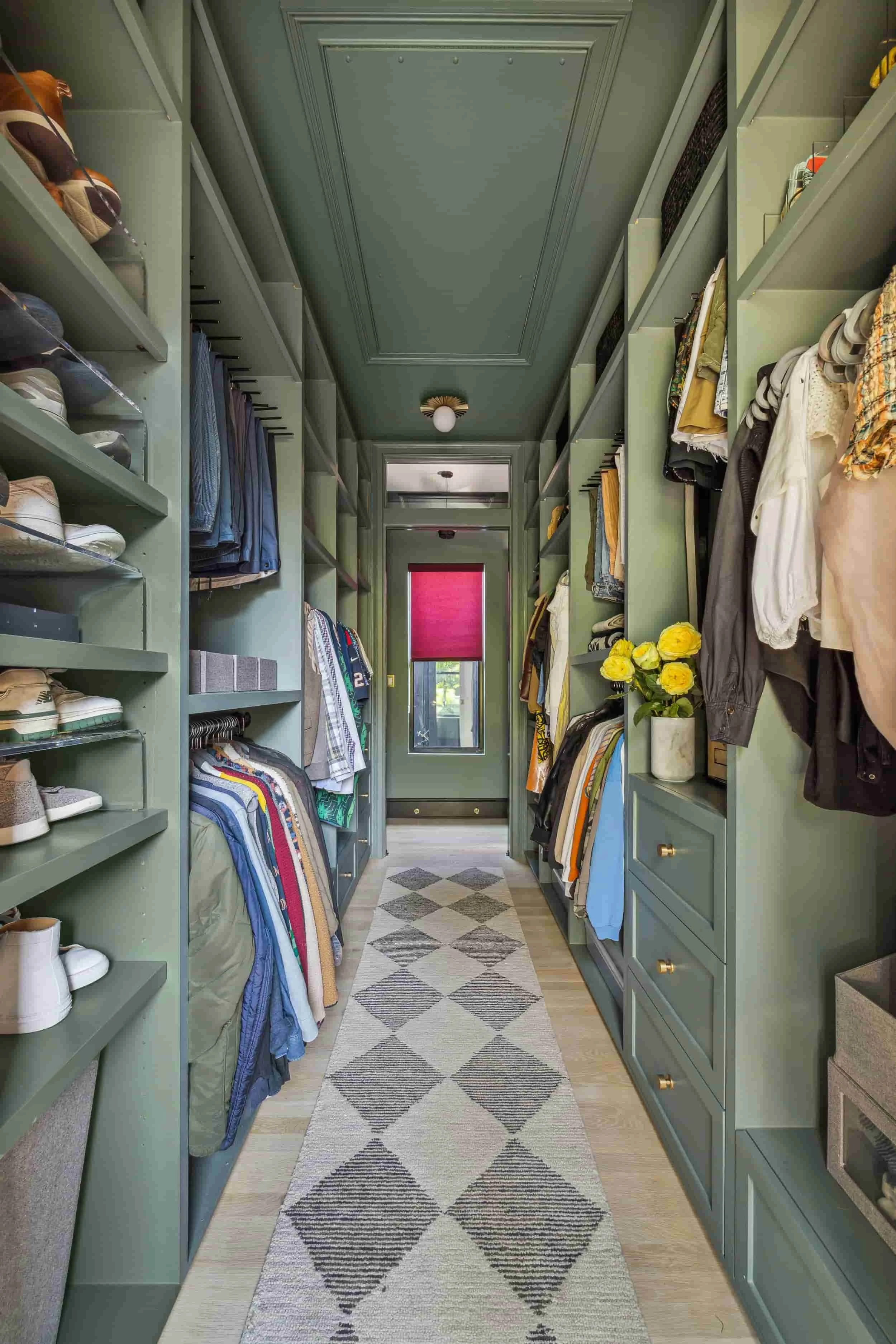 Walk-in closet designed by Hannah Goetz with sage green built-in storage, hanging clothes, and a patterned runner