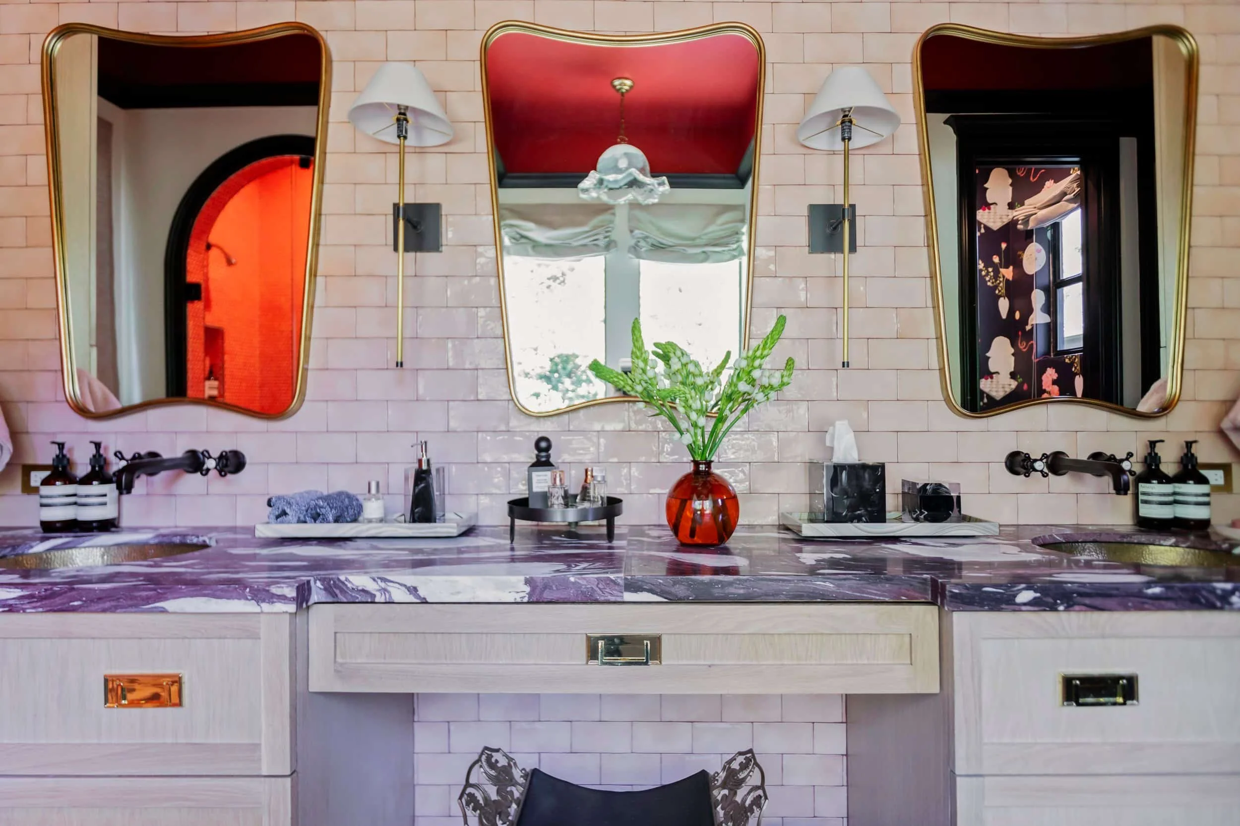 Bathroom designed by Hannah Goetz with a double vanity, purple marble countertop, pink tile, and three brass-framed mirrors.