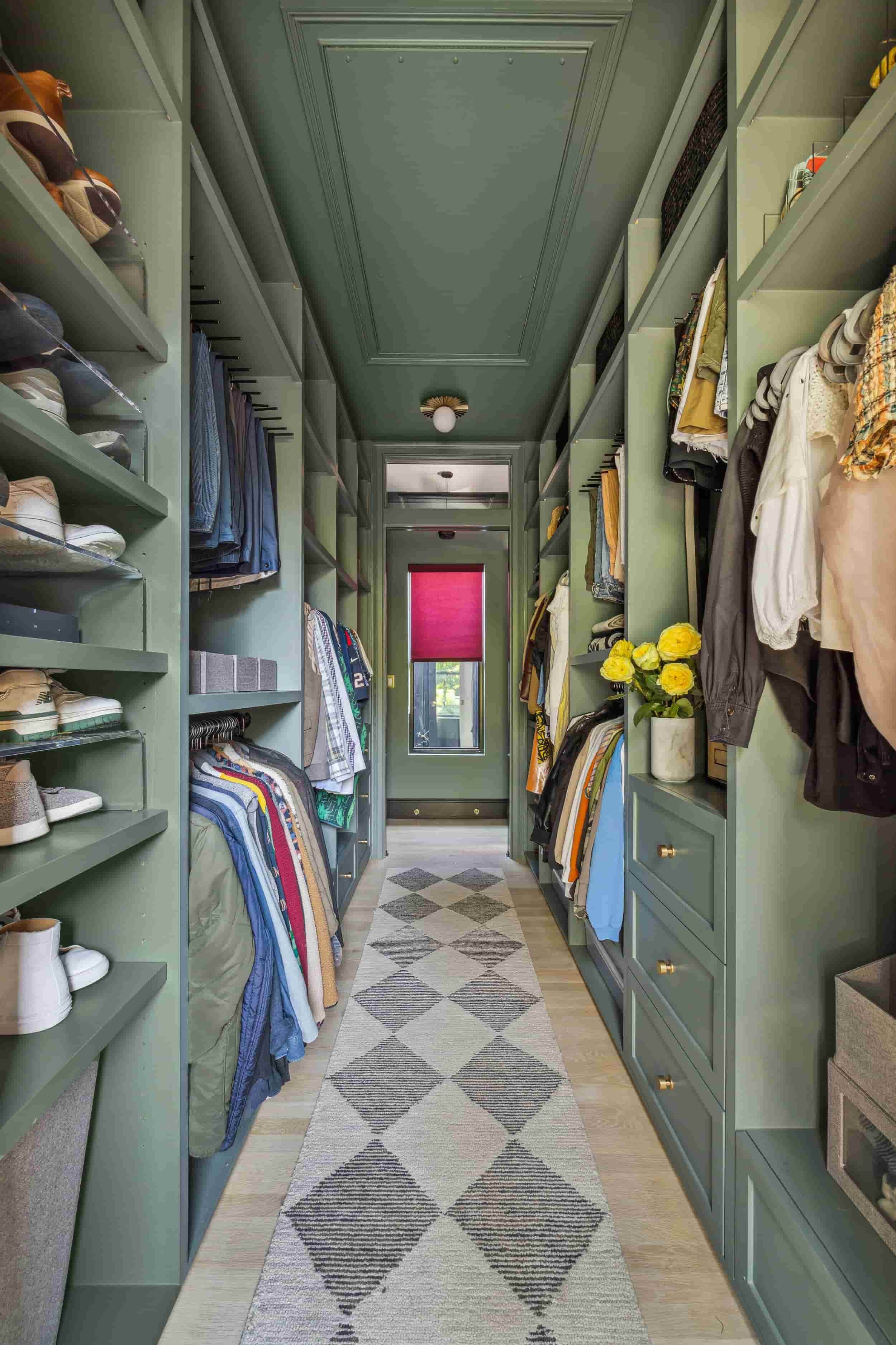 Walk-in closet designed by Hannah Goetz with sage green built-in storage, hanging clothes, and a patterned runner