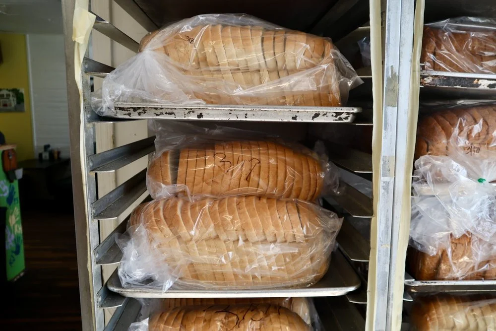 Several loaves of sliced bread wrapped in plastic on metal trays in a baking supply store.