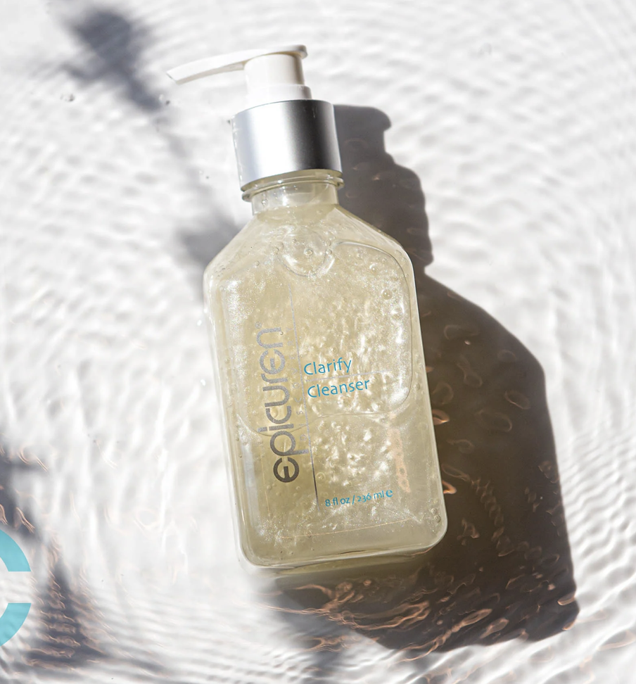 A clear plastic bottle of Gloween Clarify Cleanser with a white pump, lying on a textured white surface with sunlight creating a shadow.