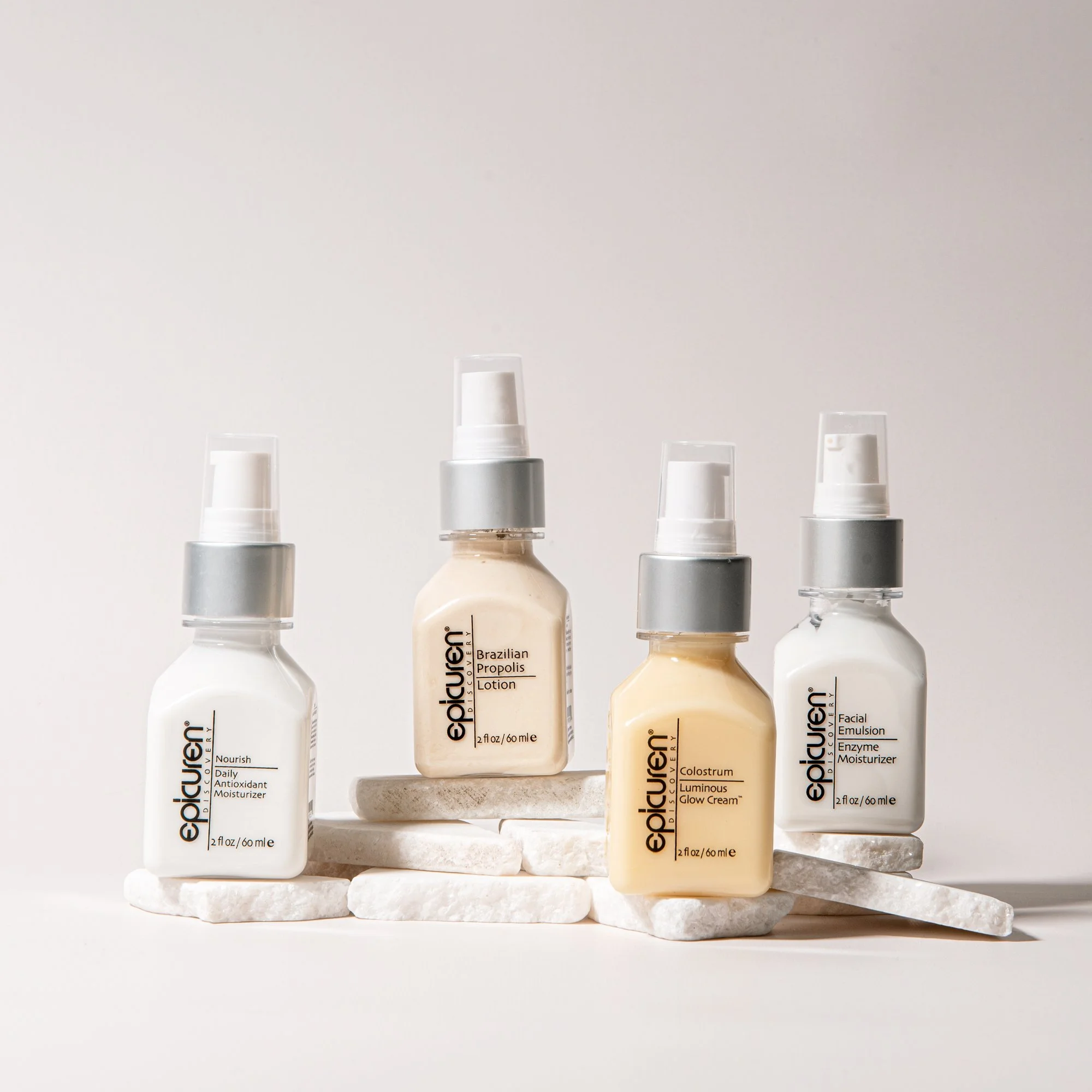 Four bottles of skincare products on white rocks against a plain background, labeled with brand Epionce and different product names.