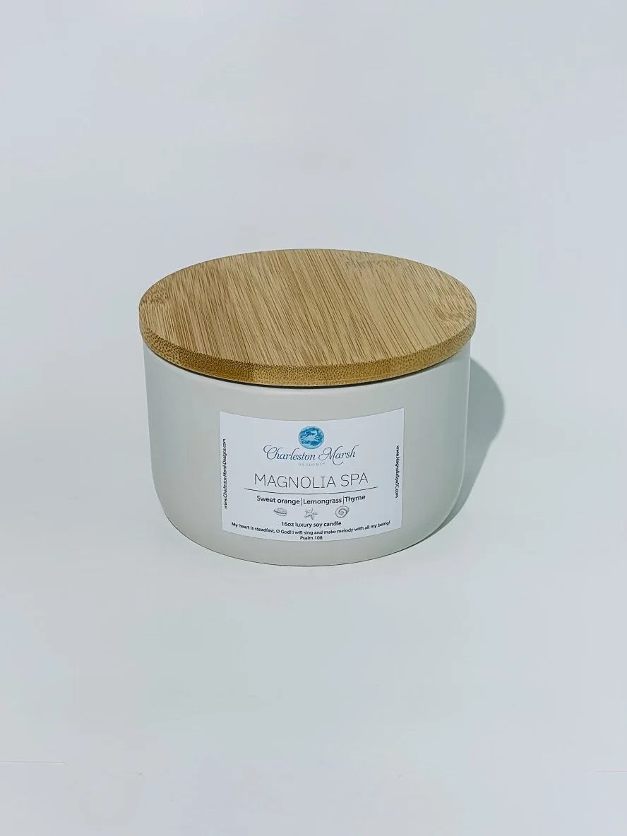 A white candle jar labeled 'Magnolia Spa' with a bamboo lid, placed on a white surface.