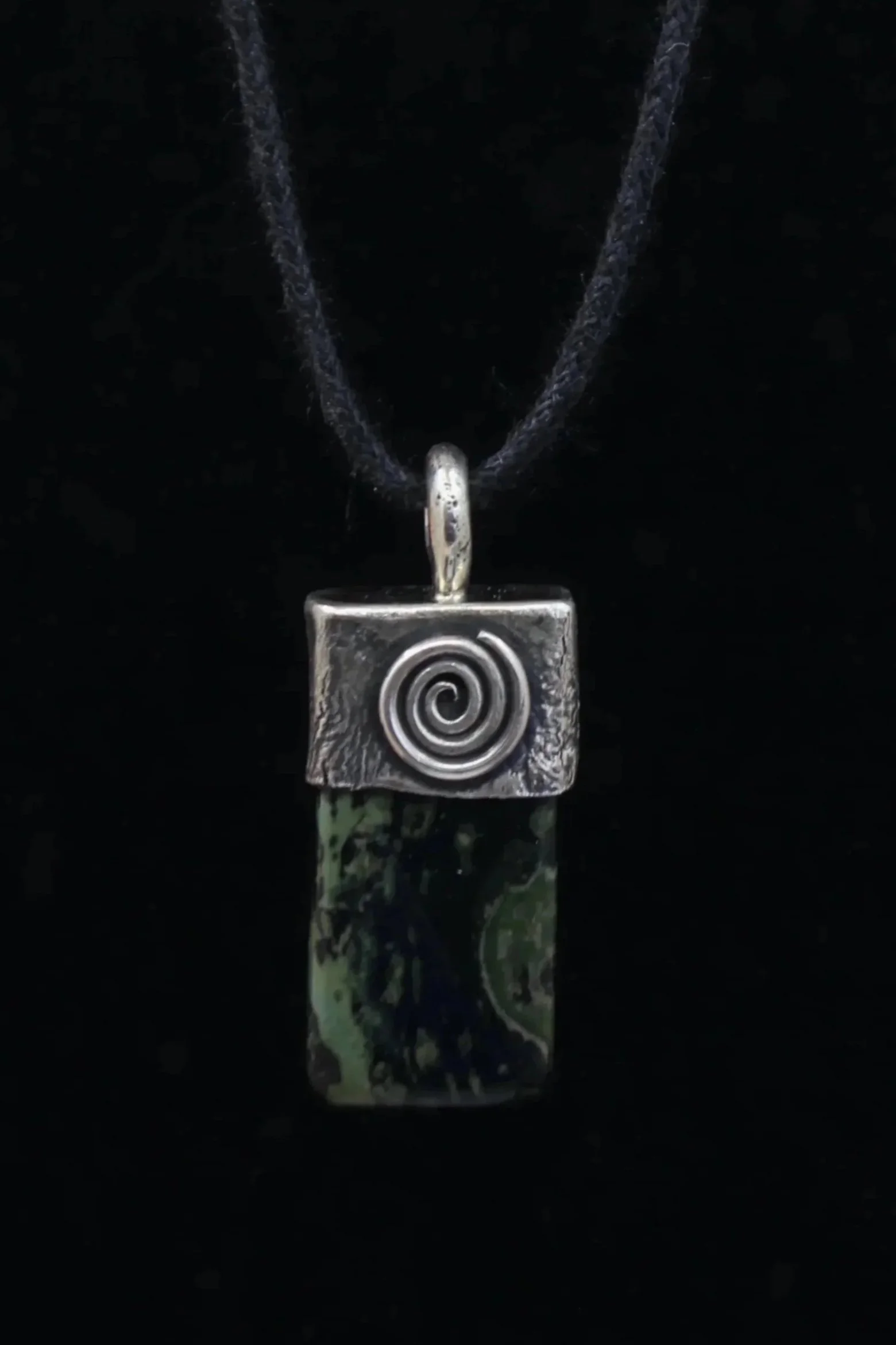 Rectangular kambaba jasper pendant whose green and black pattern is reflected in the heavy textured silver setting adorned with a raised silver spiral. 